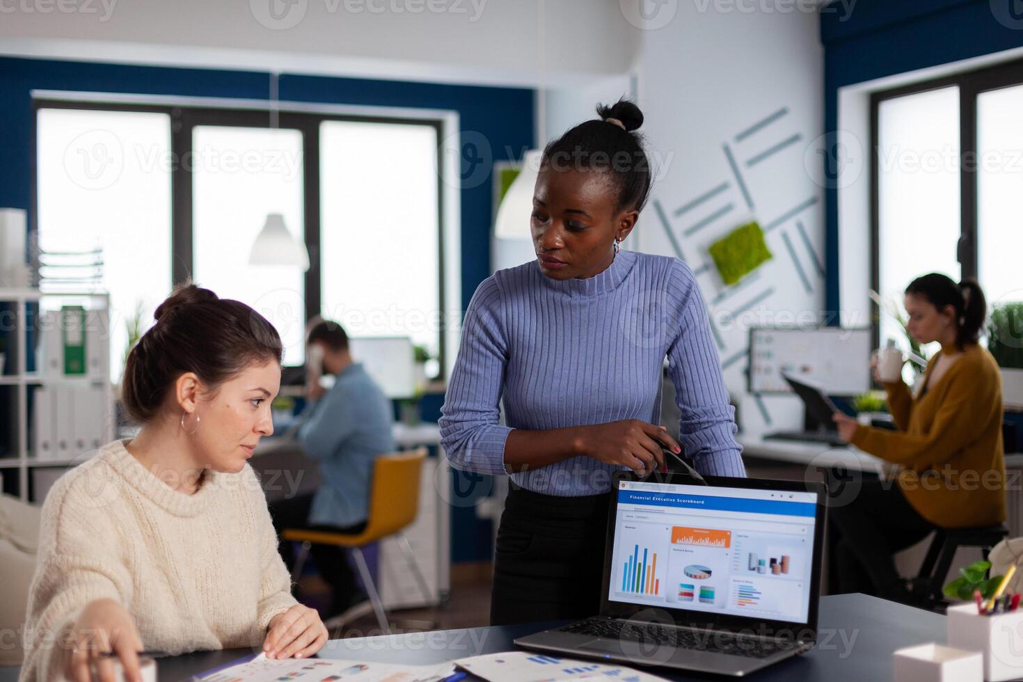 Marketing statistics analysed by diverse team colleagues of start up company. Multiethnic employees gathered in co-working space discussing financial charts. photo