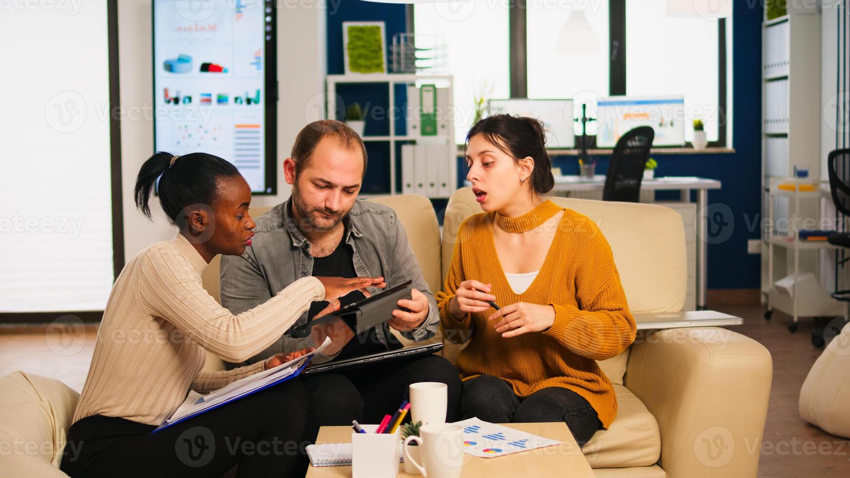 Diverse businesspeople analysing financial project during corporate meeting. Multiethnic employees group listening colleague sharing ideas discussing new marketing plan comparing data from tablet. photo