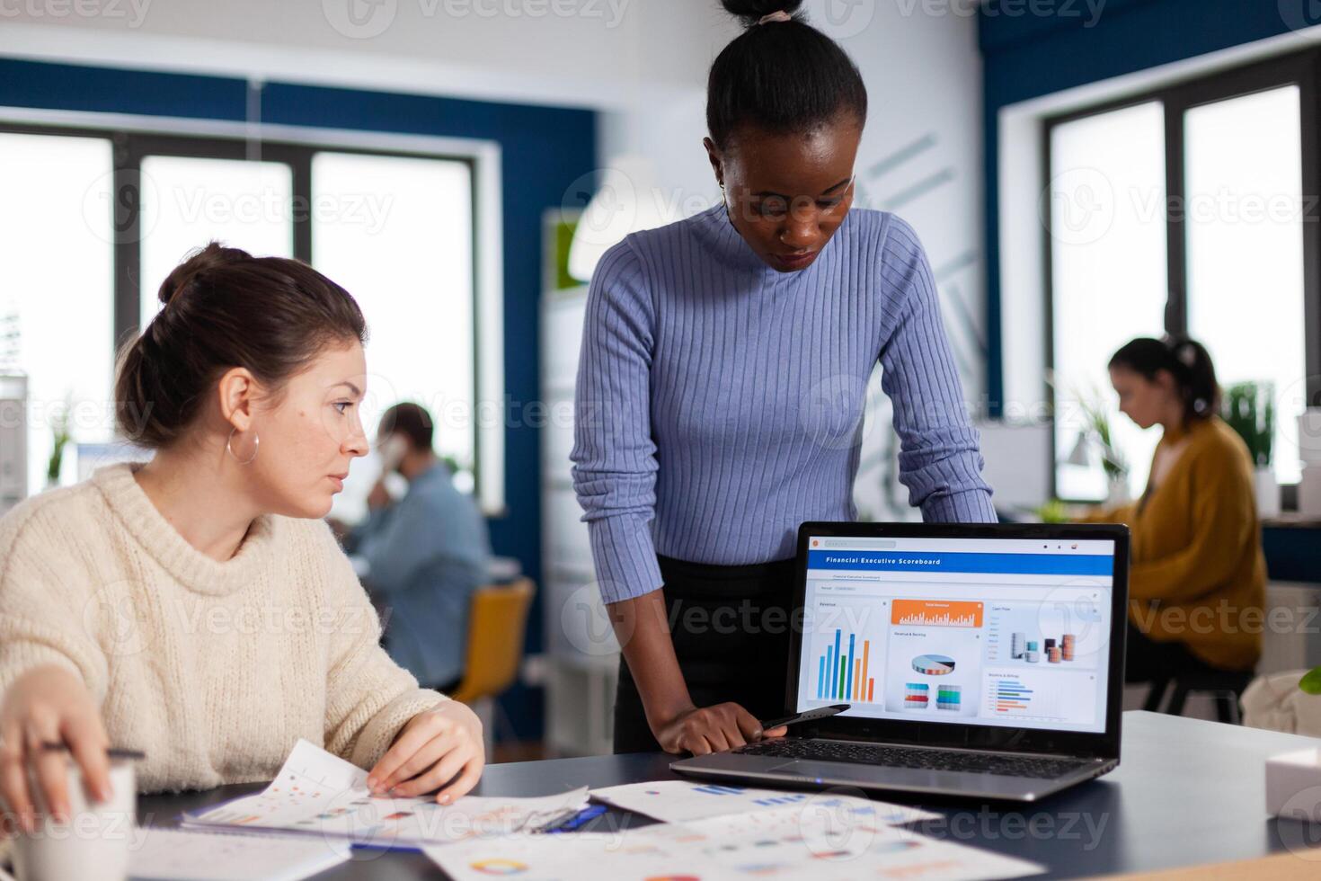 Business manager leadership briefed about financial charts by african employee looking at laptop display. Multiethnic employees gathered in co-working space. photo