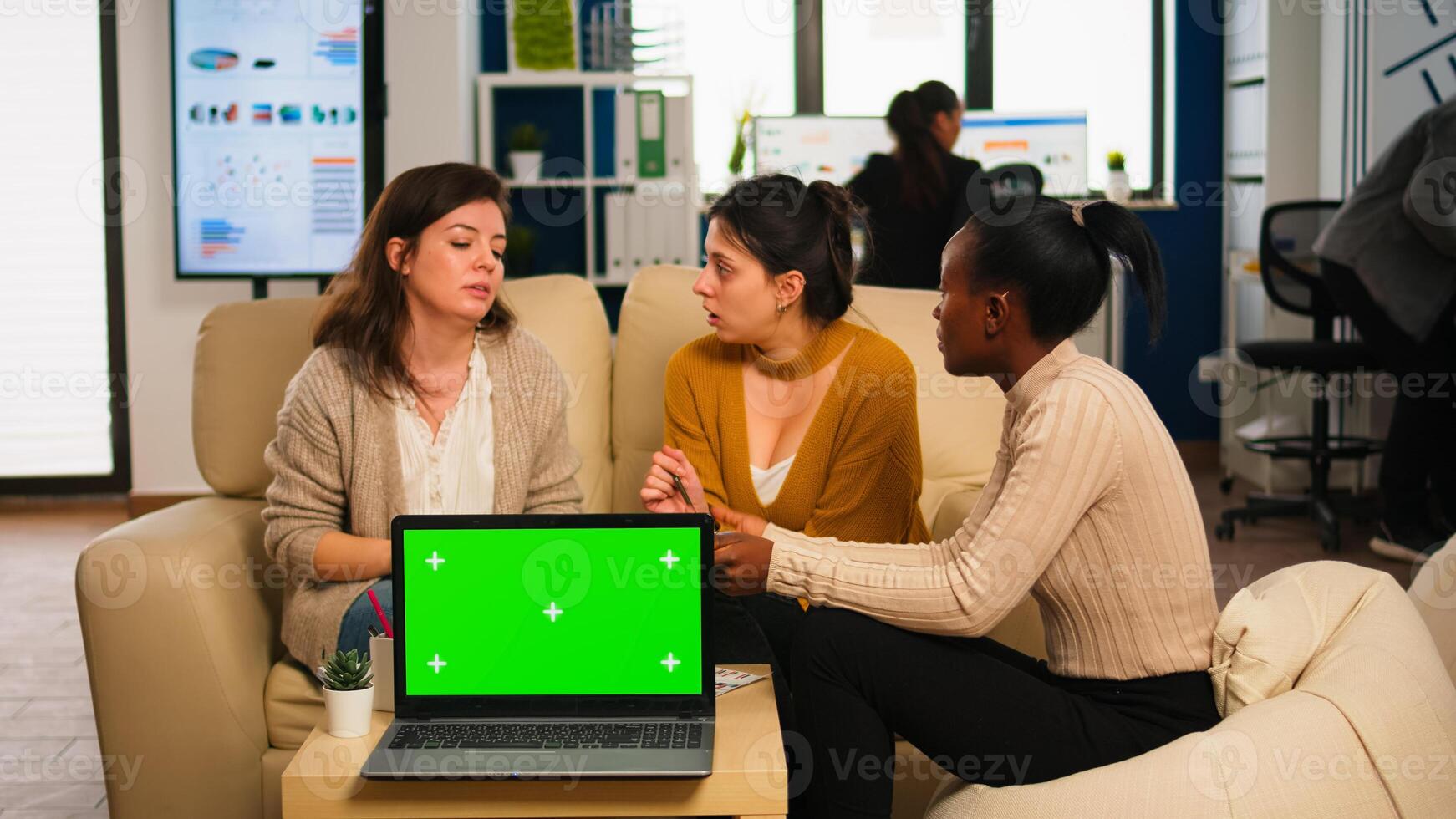 Diverse businesswomen analysing annual financial reports sitting on couch in back of laptop with green screen monitor. Leader explainig project strategy using greenscreen pc with chroma key display. photo