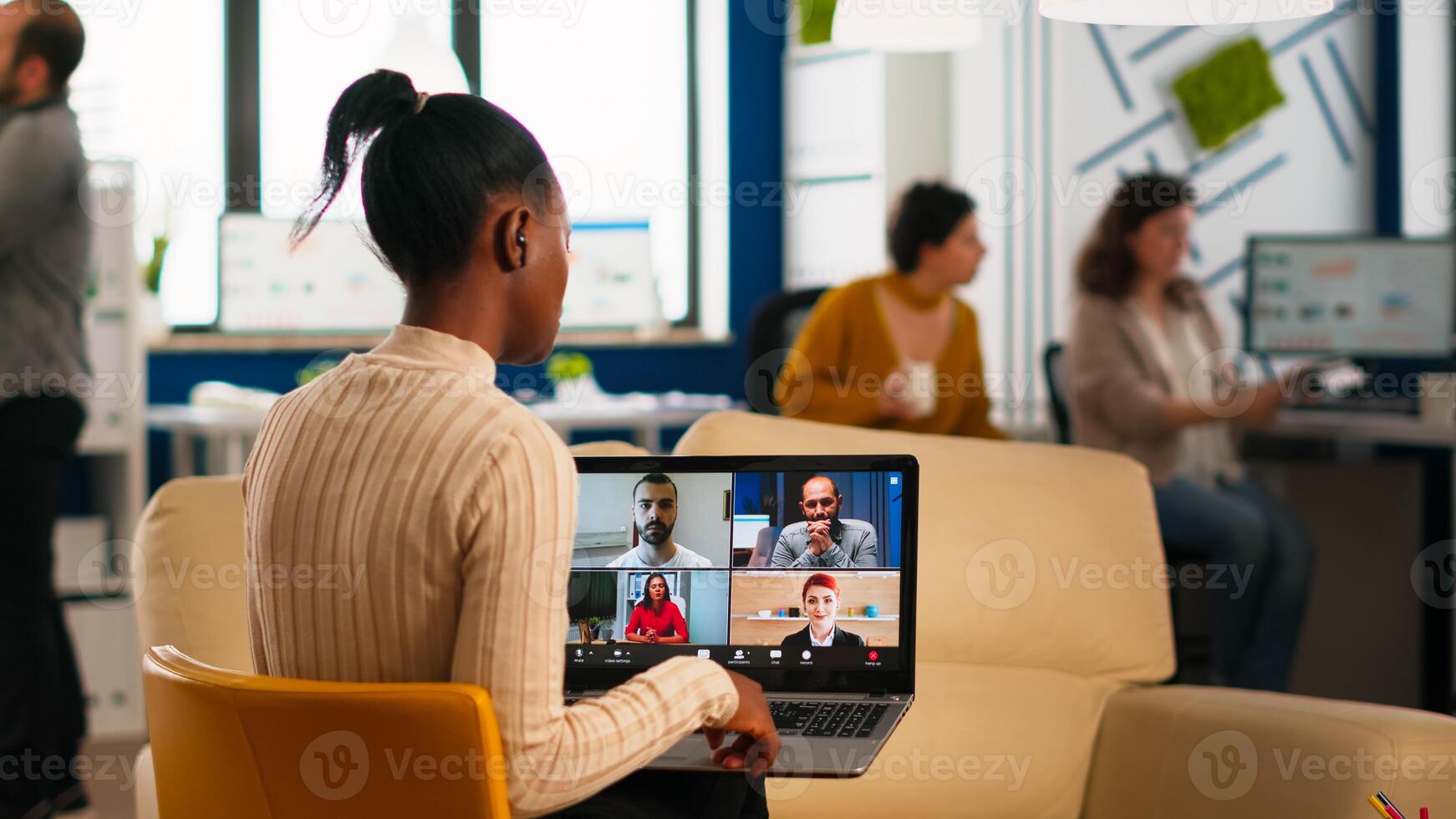African manager woman discussing with remote colleagues using call holding laptop sitting on couch in business modern office. Diverse coworkers planning new financial project in modern company photo