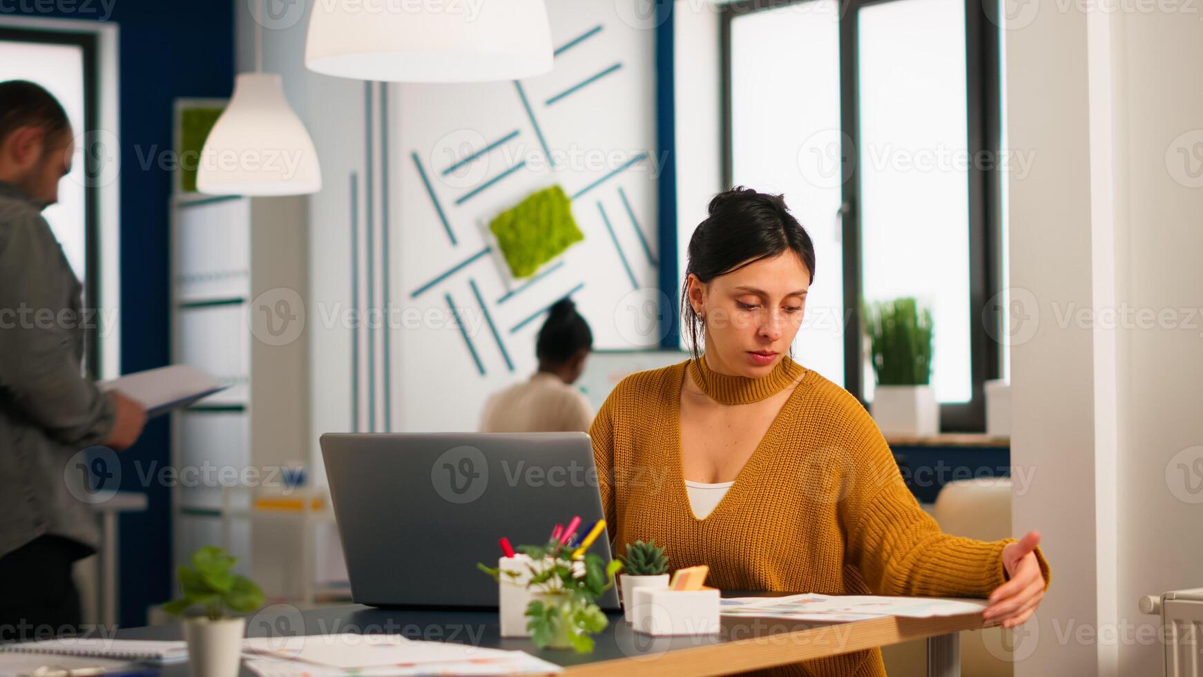 Satisfied manager checking financial statistics and graphs typing on laptop sitting at desk working in financial startup company. Diverse team analyzes statistics data in modern office photo