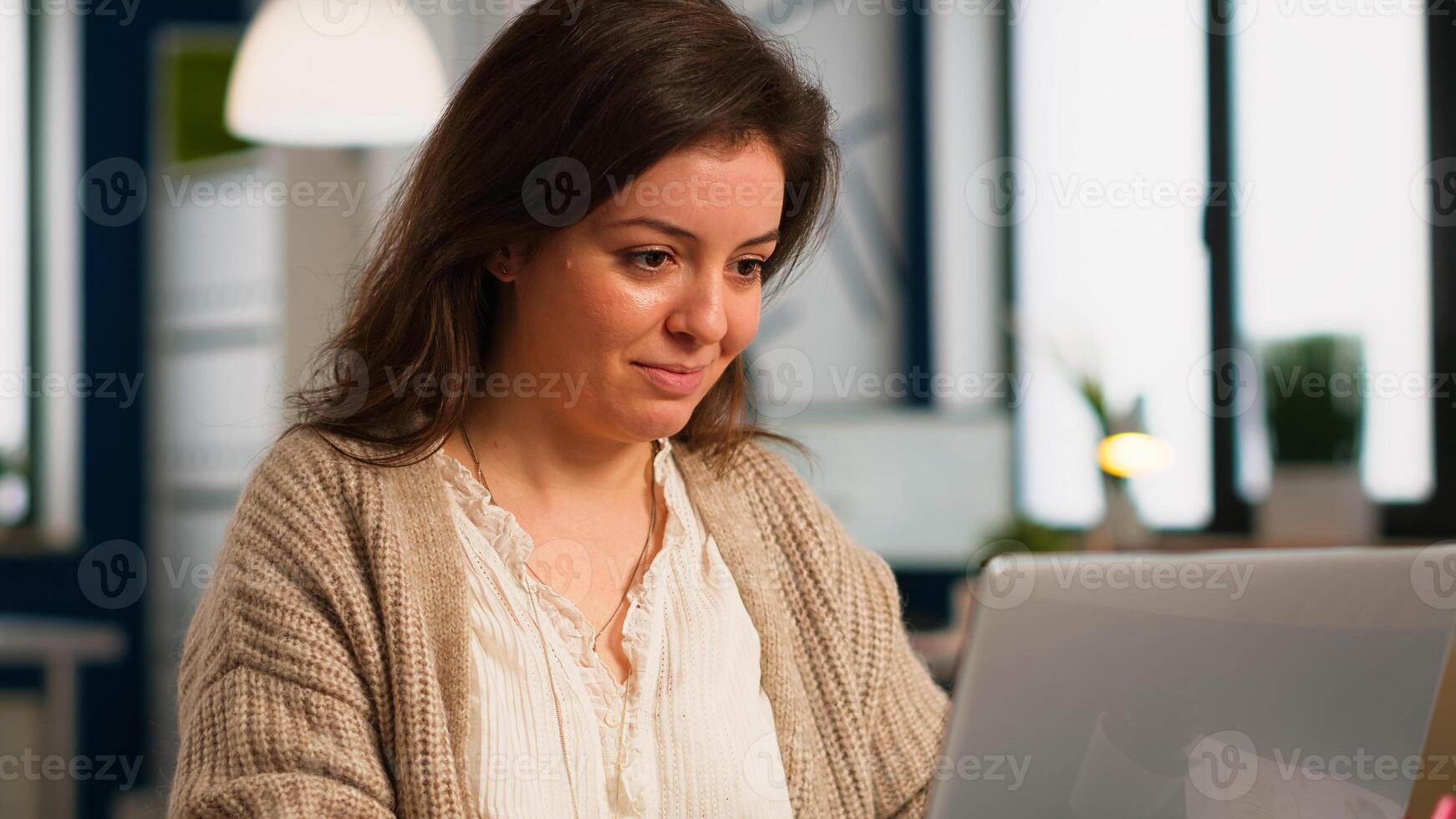 Close up of authentic happy professional employee sending mails sitting at desk in front of lapotop smiling, working financial startup company. Diverse team analyzes statistics data in modern office photo