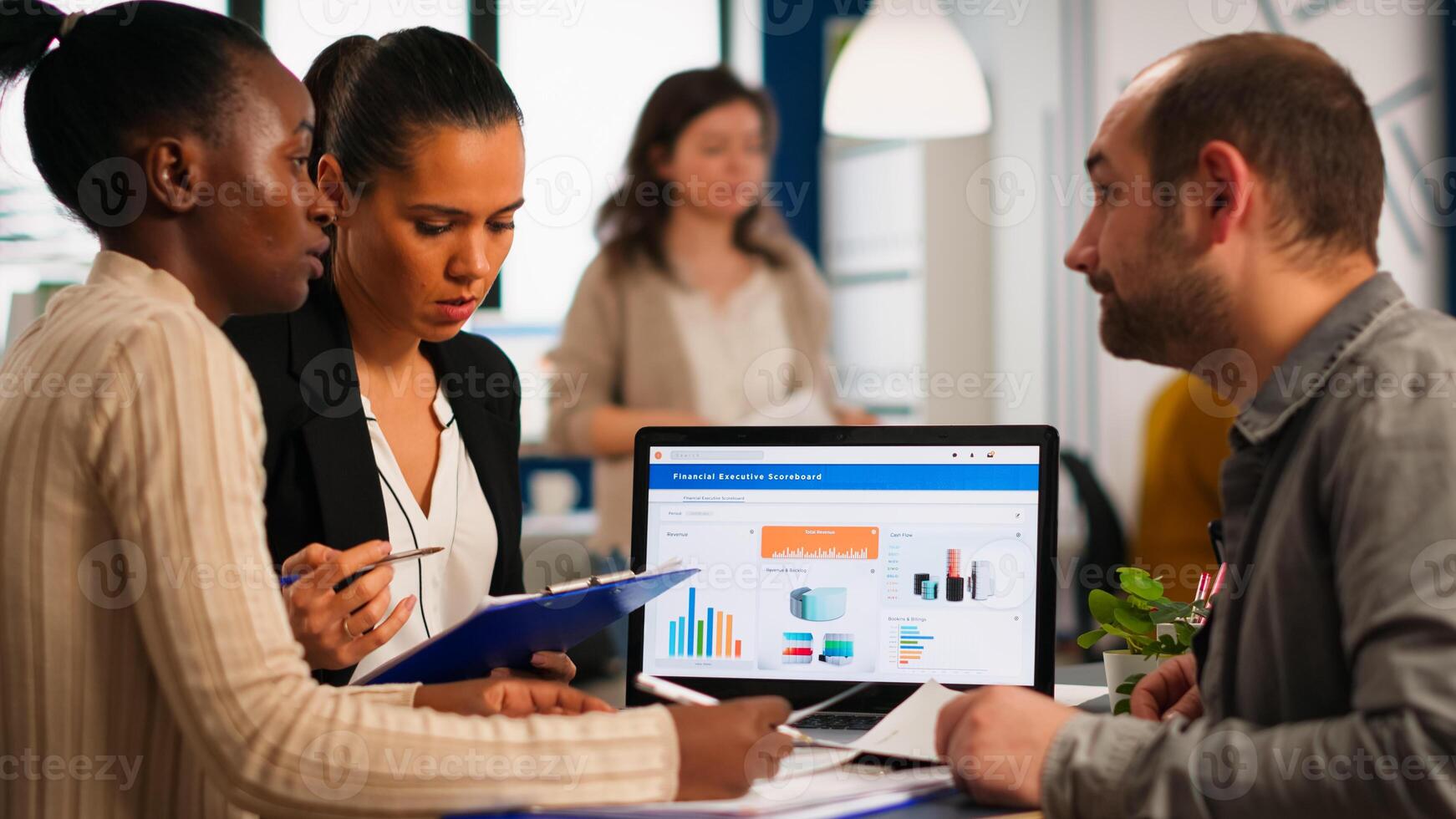 Busy multicultural, diverse employees analysing annual financial statistics sitting at desk in front of laptop holding documents searching business solutions. Team of businesspeople working in company photo
