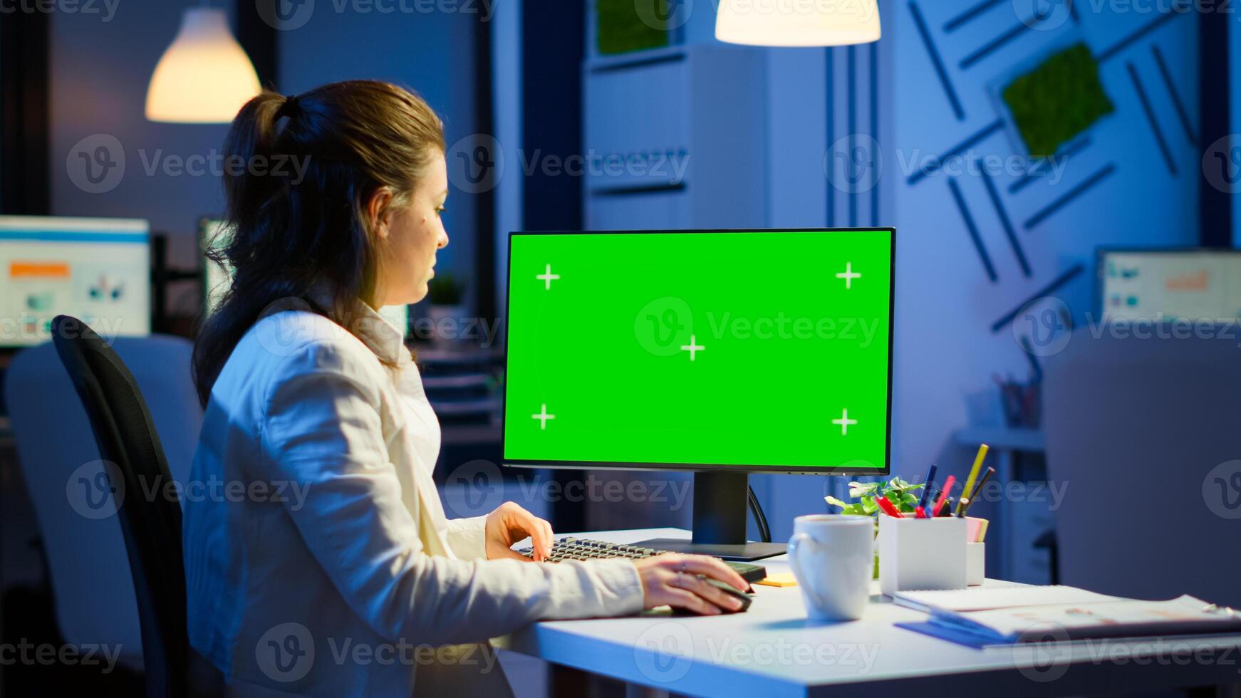 Woman looking at computer with chroma key during night time in start up business office working overtime. Freelancer watching desktop monitor mockup display with green screen, typing writting photo