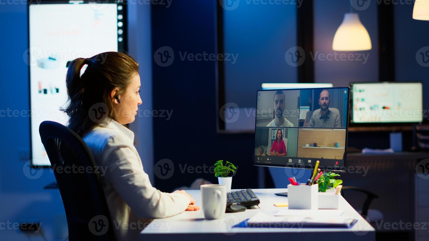 Businesswoman talking during conference with team in midnight using pc in start up business office. Corporate meeting using technology network wireless discussing on webcam late at night photo