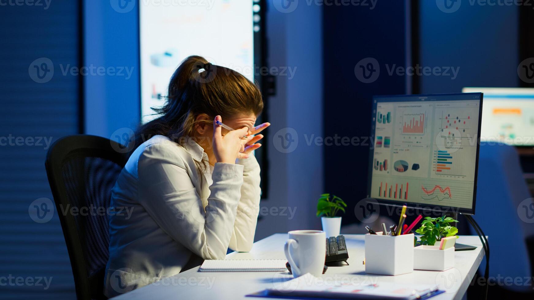 Focused tired entrepreneur checking graphics from laptop writing on notebook working from business office overtime. Busy employee using modern technology network wireless reading typing, searching photo
