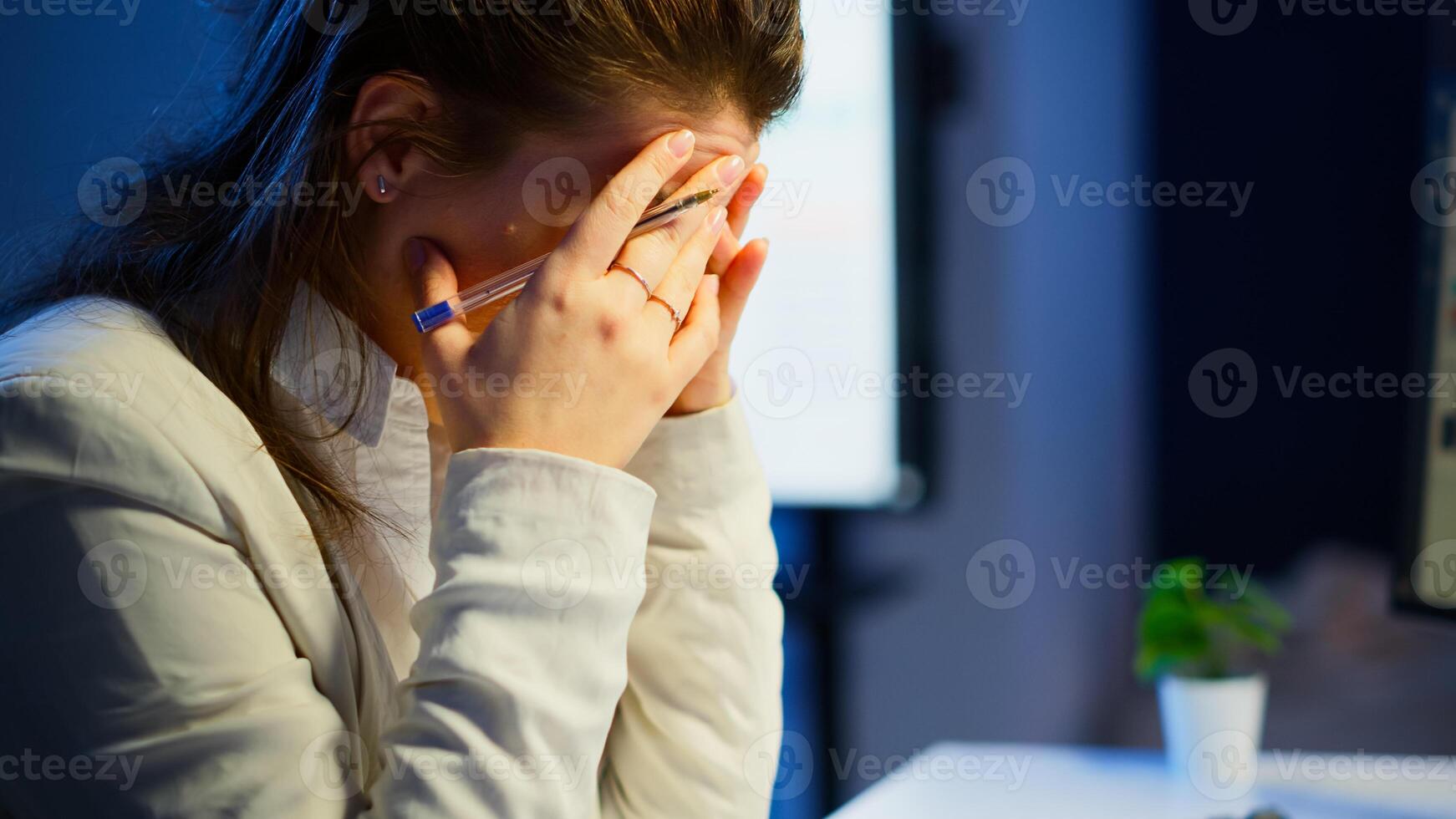Close up of stressed busy woman with headache working from business office late at night. Tired focused employee using modern technology network wireless doing overtime for job checking reports photo