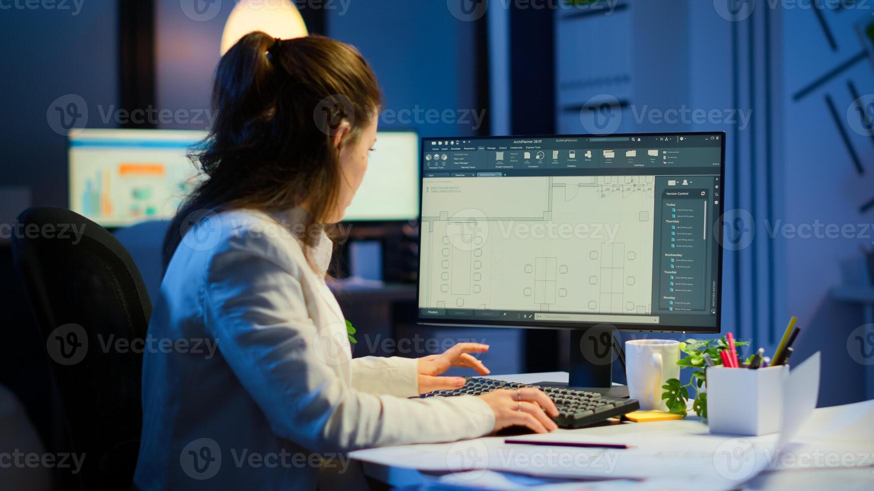 Woman architect matching digital plans from pc with blueprints working in start-up business office overtime. Designer using cad software to design a 3D concept of buildings creating late at night photo