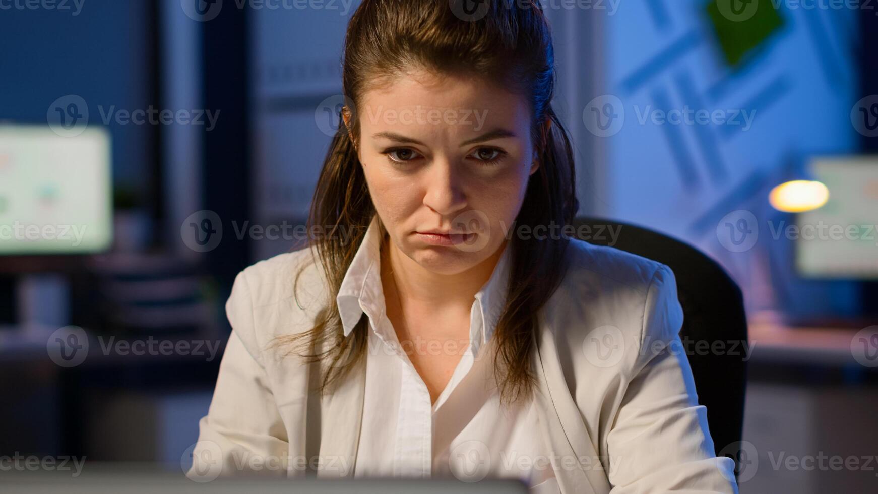 Close up of exhausted manager working overtime to respect deadline of project sitting in business office typing on laptop late at night. Focused employee using modern technology network wireless photo