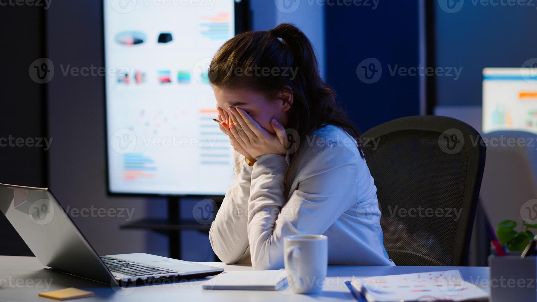 Exhausted freelancer sleeping in front of laptop working in modern start up company office late at night. Stressed employee using modern technology network wireless doing overtime closing eyes. photo