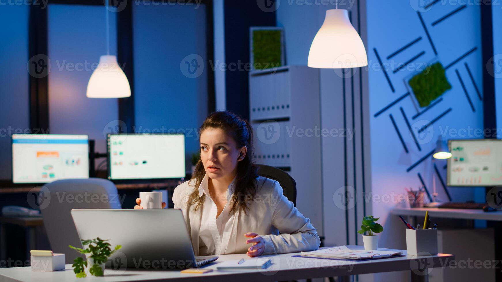 Manager speaking online with remotely coworkers late at night sitting in busineess office at laptop in midnight. Employee using technology network wireless talking on virtual meeting doing overtime photo