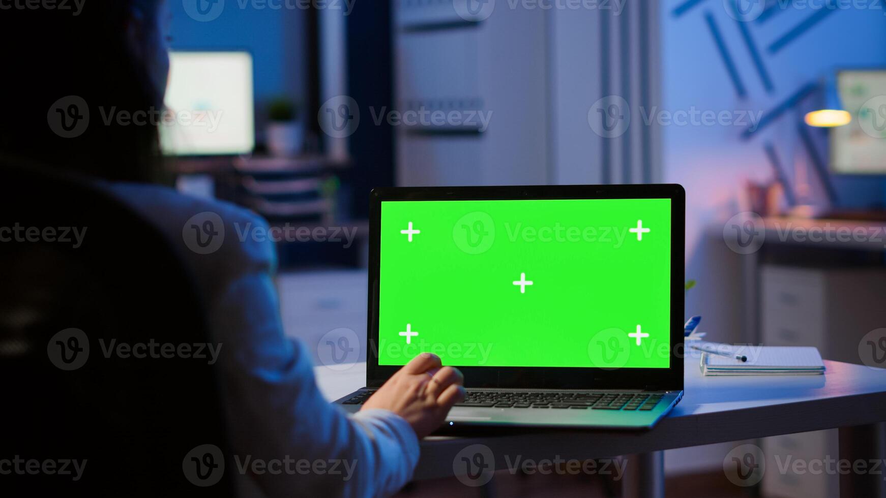 Woman looking at laptop with green mockup during night time in start up business office working overtime. Freelancer watching desktop monitor display with green screen, chroma key, typing writting photo