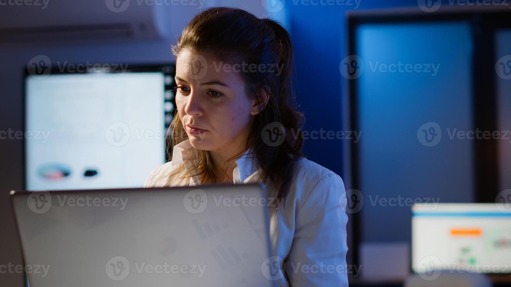 Freelancer typing on laptop late at night standing in start up business office late at night working. Busy focused employee using modern technology network wireless doing overtime for job searching photo