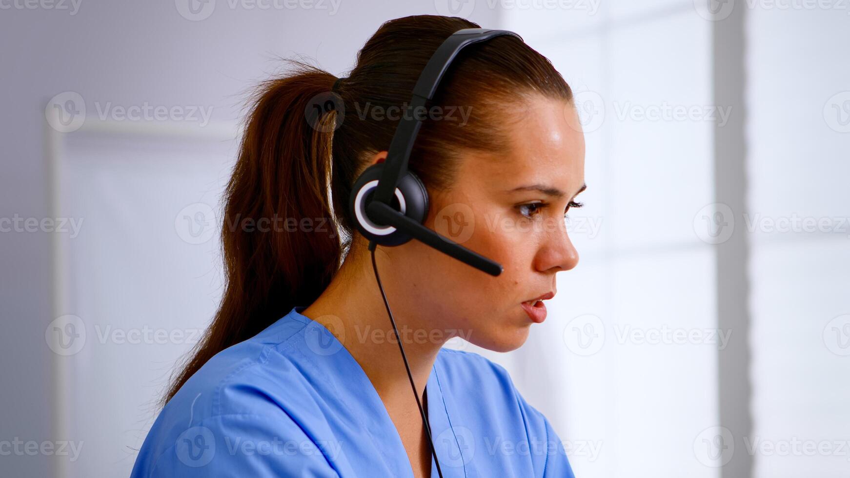 Portrait of medical receptionist answering pressing on headphone helping patient making appointment in hospital. Healthcare physician in medicine uniform, doctor assistant during telehealth communication photo