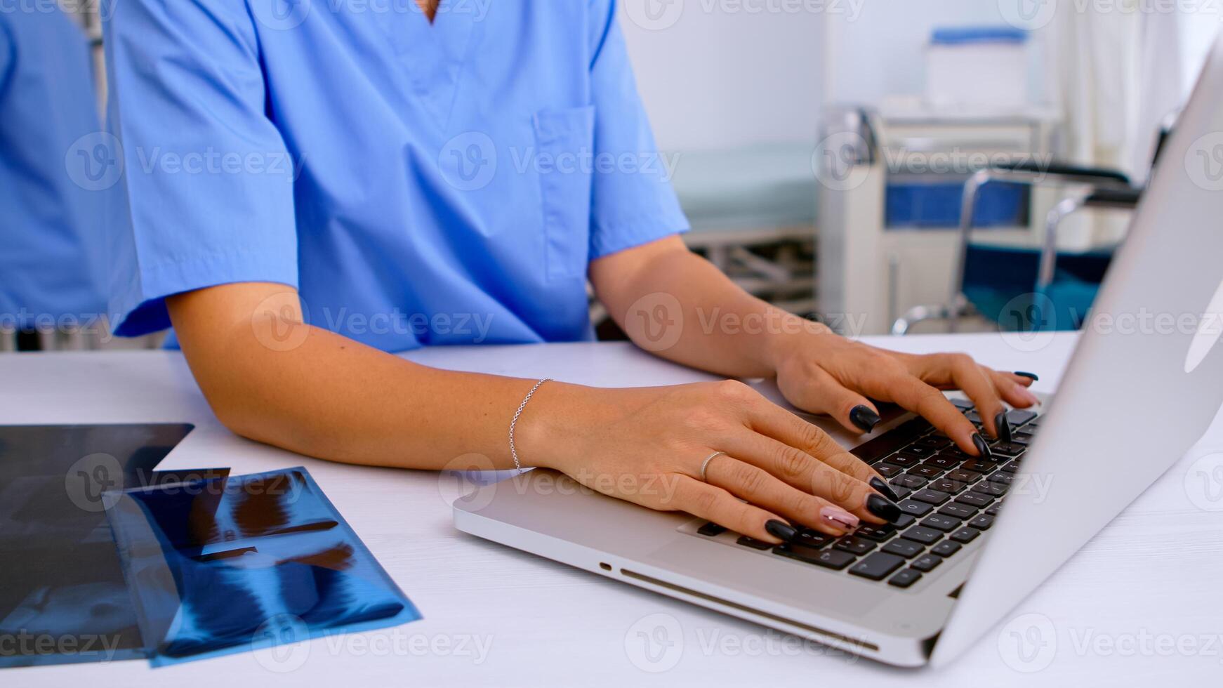 Close up of medical woman nurse writing results of patient radiography, typing on laptop sitting in hospital. Radiologist in medical uniform looking at x-ray, examination, bone, analyze, diagnosis. photo