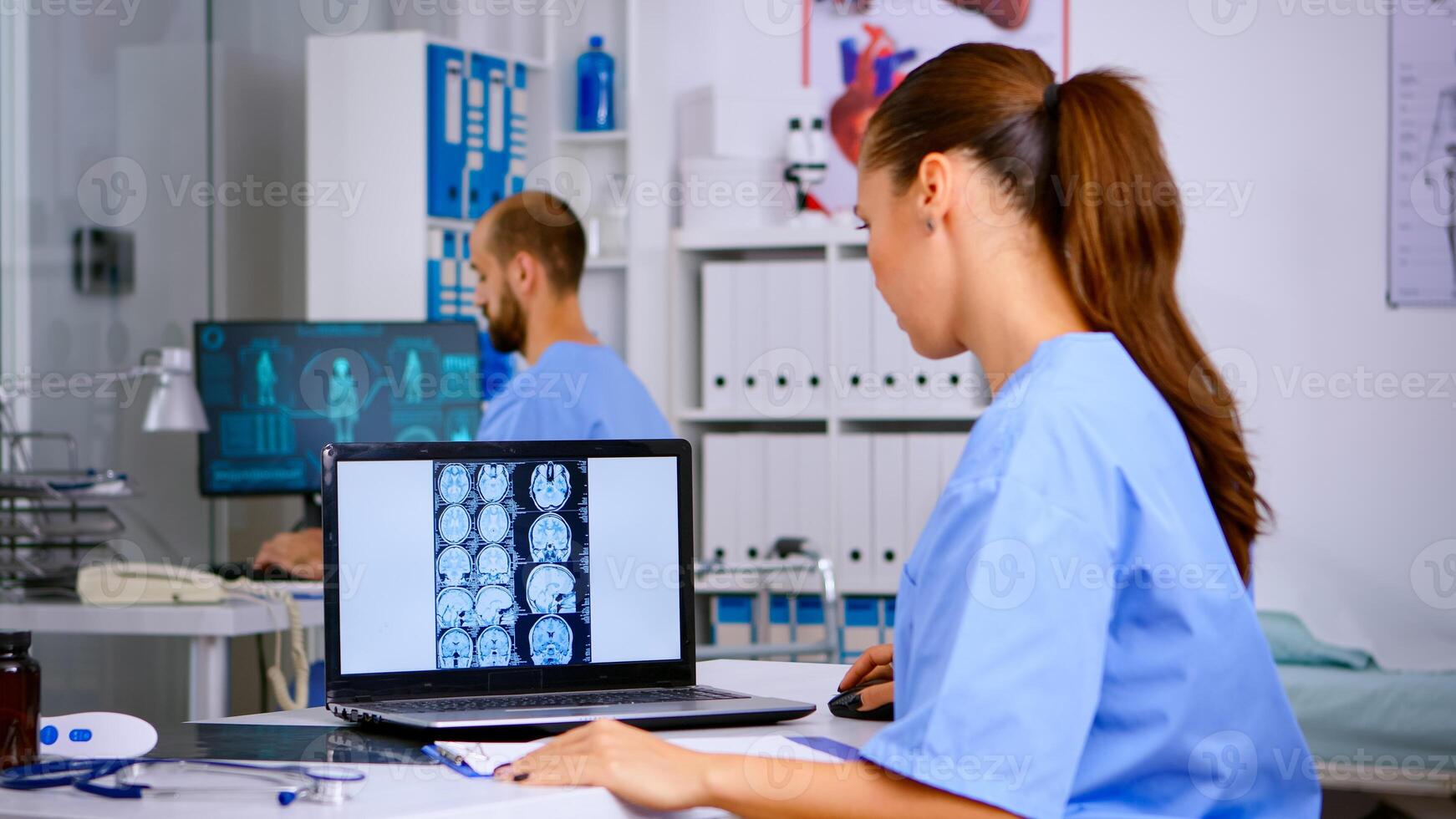 Doctor assistant analyzing skull brain x-ray tommography medical data on laptop, taking notes on clipboard. Radiologist in medicine uniform looking at digital radiography, examination, diagnosis. photo