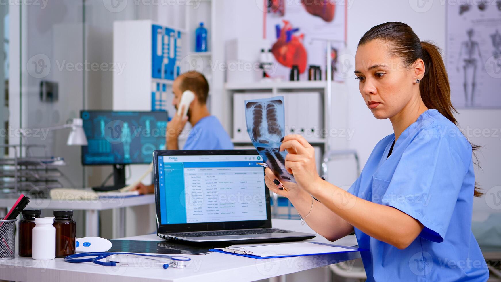 Medical doctor nurse holding and analysing radiography checking treatment of diagnosed patients, writing informations in laptop. Assistant working in hospital making appointments and registration. photo