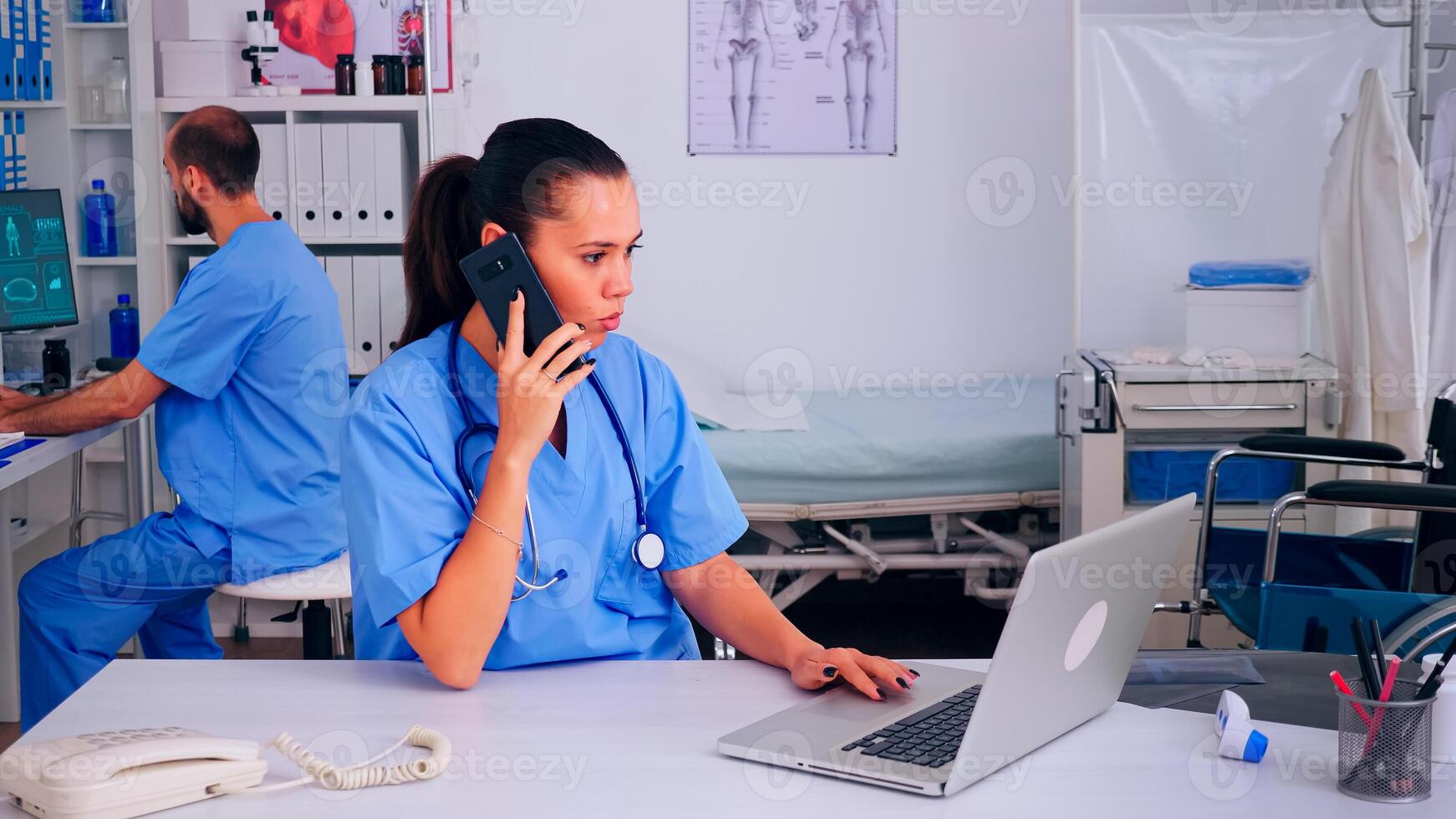 Nurse physician consulting remote patient using smartphone in hospital wearing medicine uniform. Doctor healthcare assistant helping patient with telehealth communication, diagnosing, typing on laptop photo