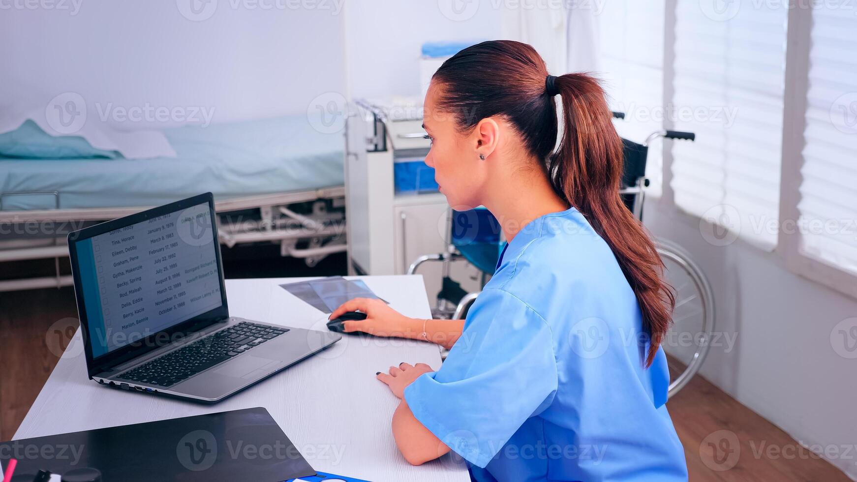 Nurse of doctor typing on laptop sitting at desk in cabinet, analysing appointments of patients. Medical physician in medicine uniform writing list of consulted, diagnosed patients, making research. photo