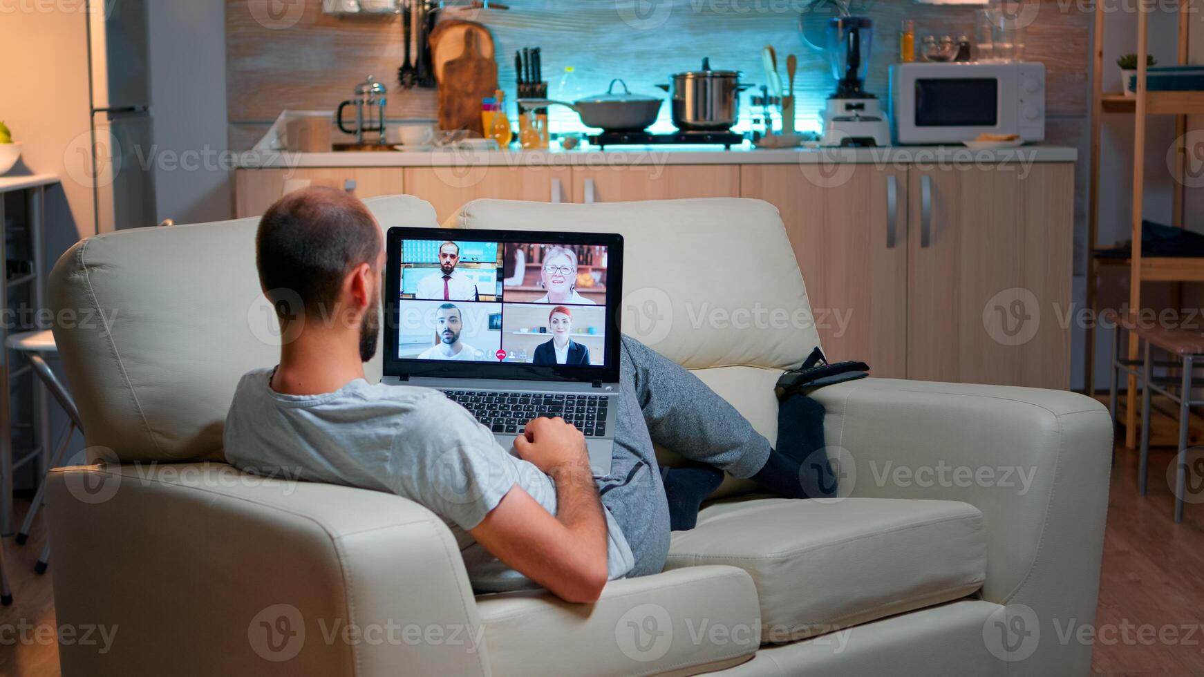 Caucasian male talking with collegues during call conference using laptop computer with modern technology wireless. Tired man relaxing on sofa late at night in kitchen photo