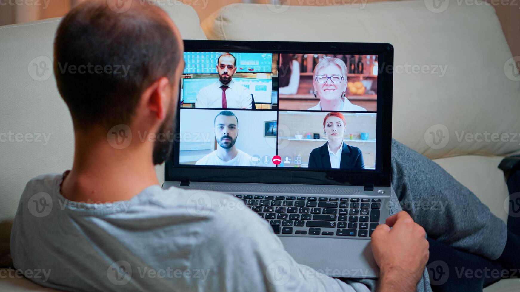 Focused adult using laptop computer during videocall conference talking about social business connection while sitting on couch. Relaxed man working at online communication project overtime in kitchen photo