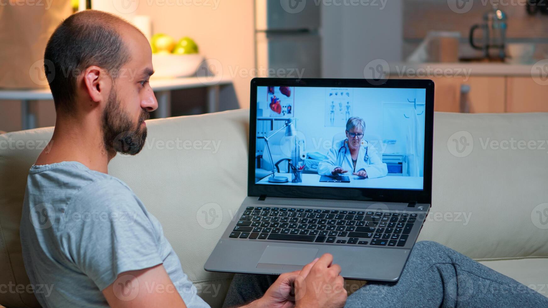 Caucasian male chatting with physician doctor during online telemedicine consultation sitting in home kitchen. Sick man disscusing about illness symptoms and headlcare treatment photo