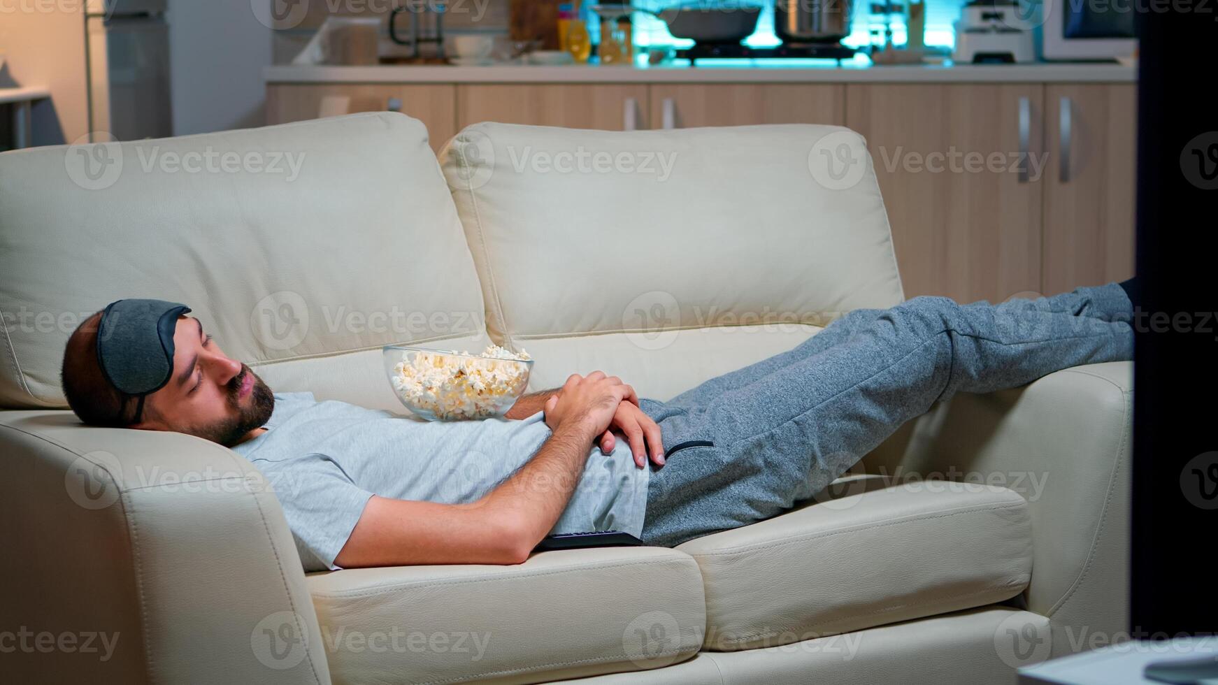 Man closing his eye and falling asleep on the couch in living room in front of the TV, while the television entertainment is ON. Relaxation cinema after a hard week of work photo