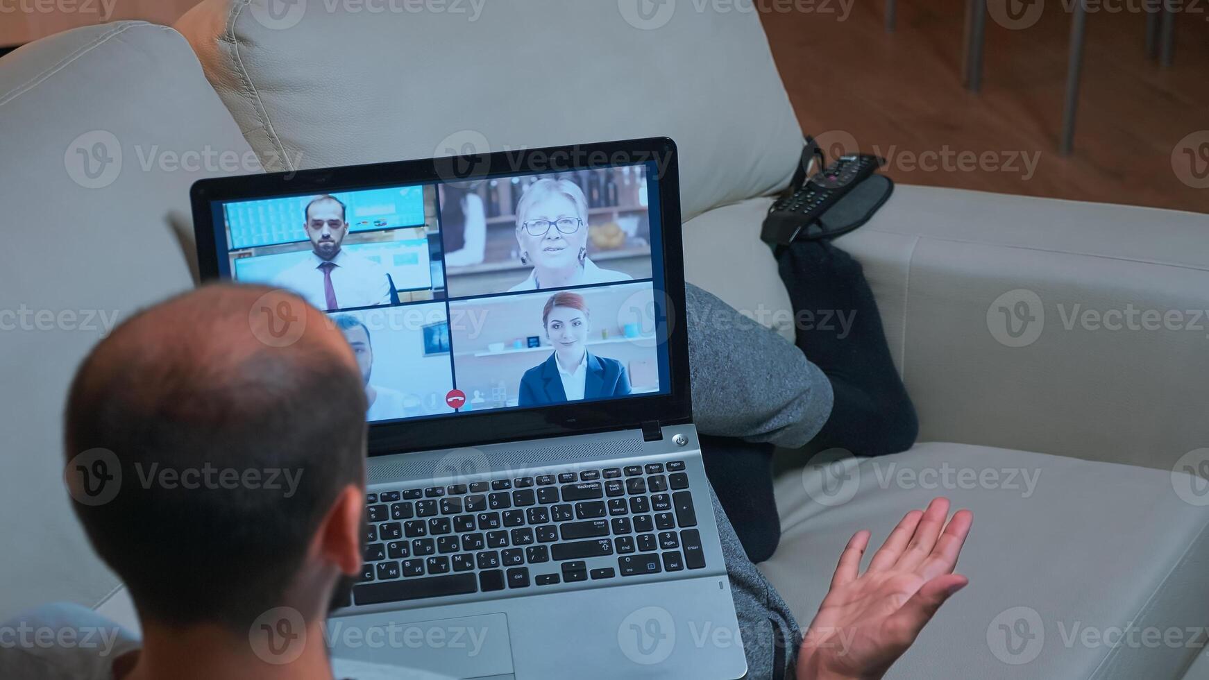 Back shot of tired man lying on sofa while chatting with teammates during business videocall conference use laptop computer. Caucasian male using modern technology wireless late at night in kitchen photo