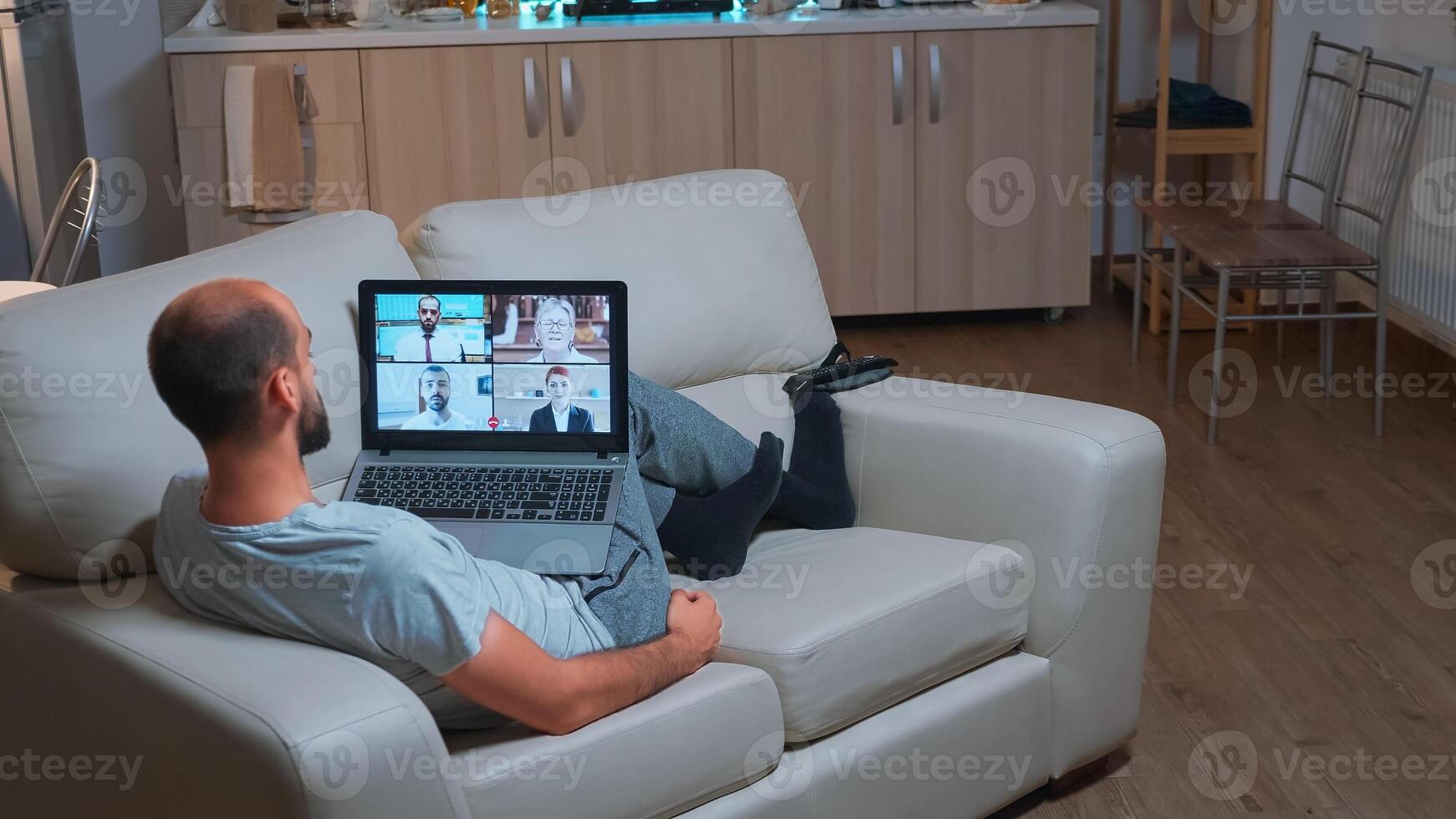 Caucasian male talking about business communication project during call meeting use laptop computer. Focused man lying on sofa in pijamas using modern technology wireless late at night photo