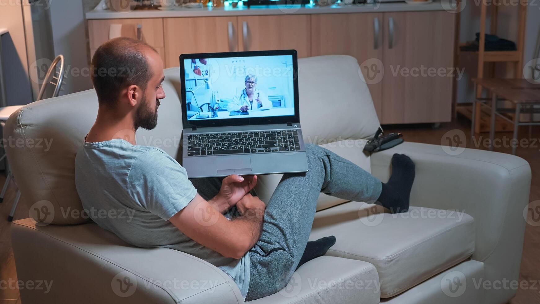 Doctor consulting sick patient during coronavirus quarantine using laptop computer for videocall consultation sitting on sofa. Caucasian man disscusing about illness symptoms and headlcare treatment photo