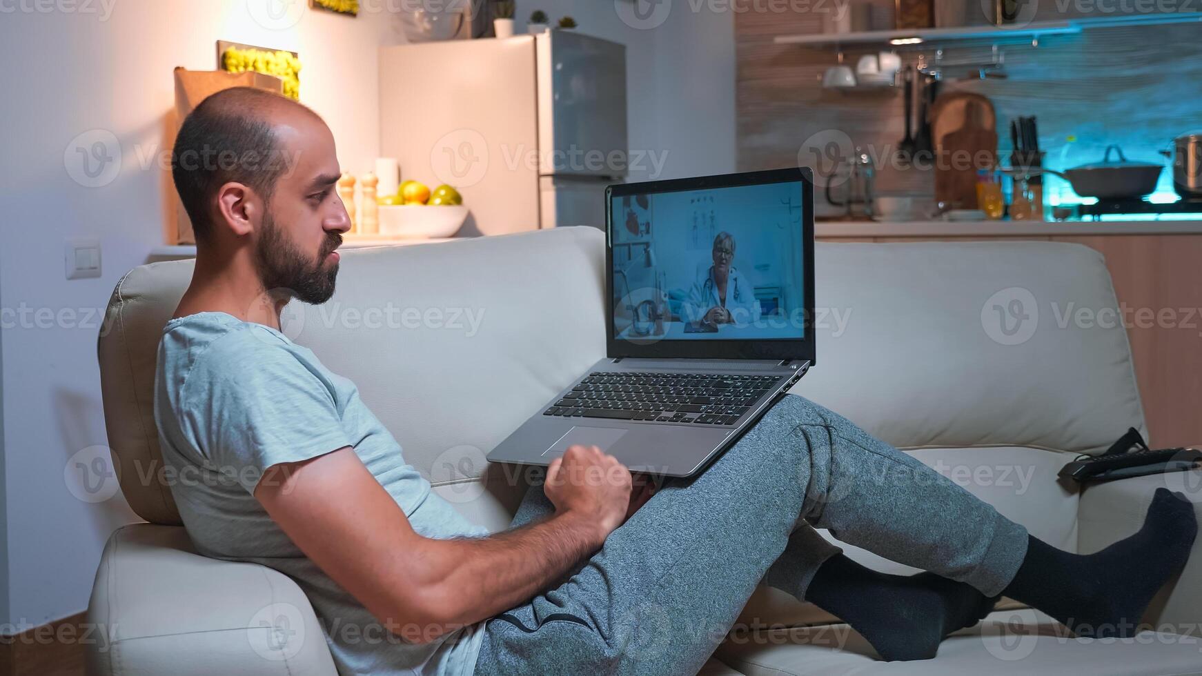 Physician doctor consulting sick patient during videocall consultation using laptop computer while standing on sofa. Caucasian man talking about illness symptoms and headlcare treatment photo