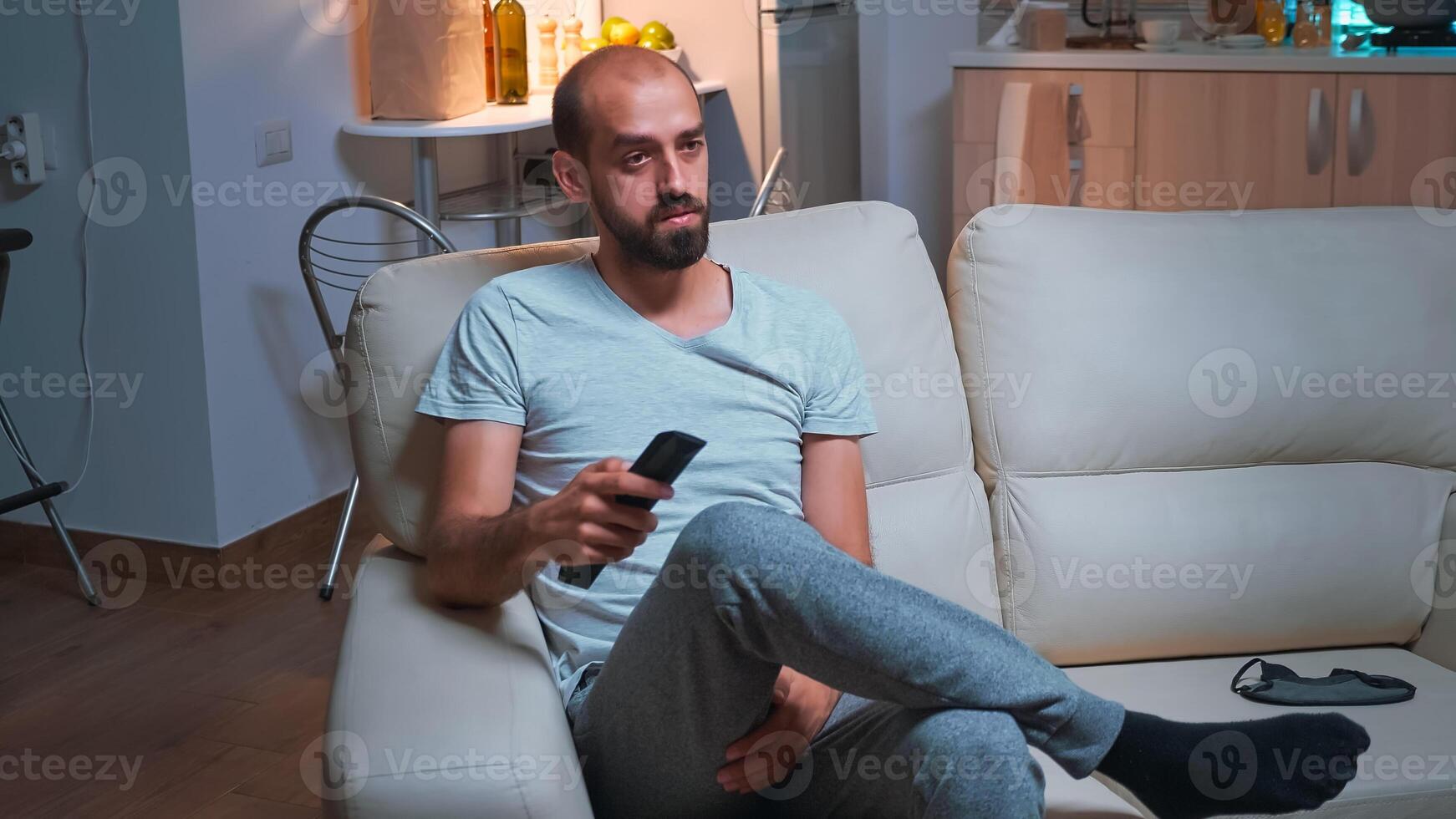 Portrait of concentrated man watching entertainment shows series sitting on couch in front of television. Caucasian male relaxing after long day at work late at night in kitchen photo