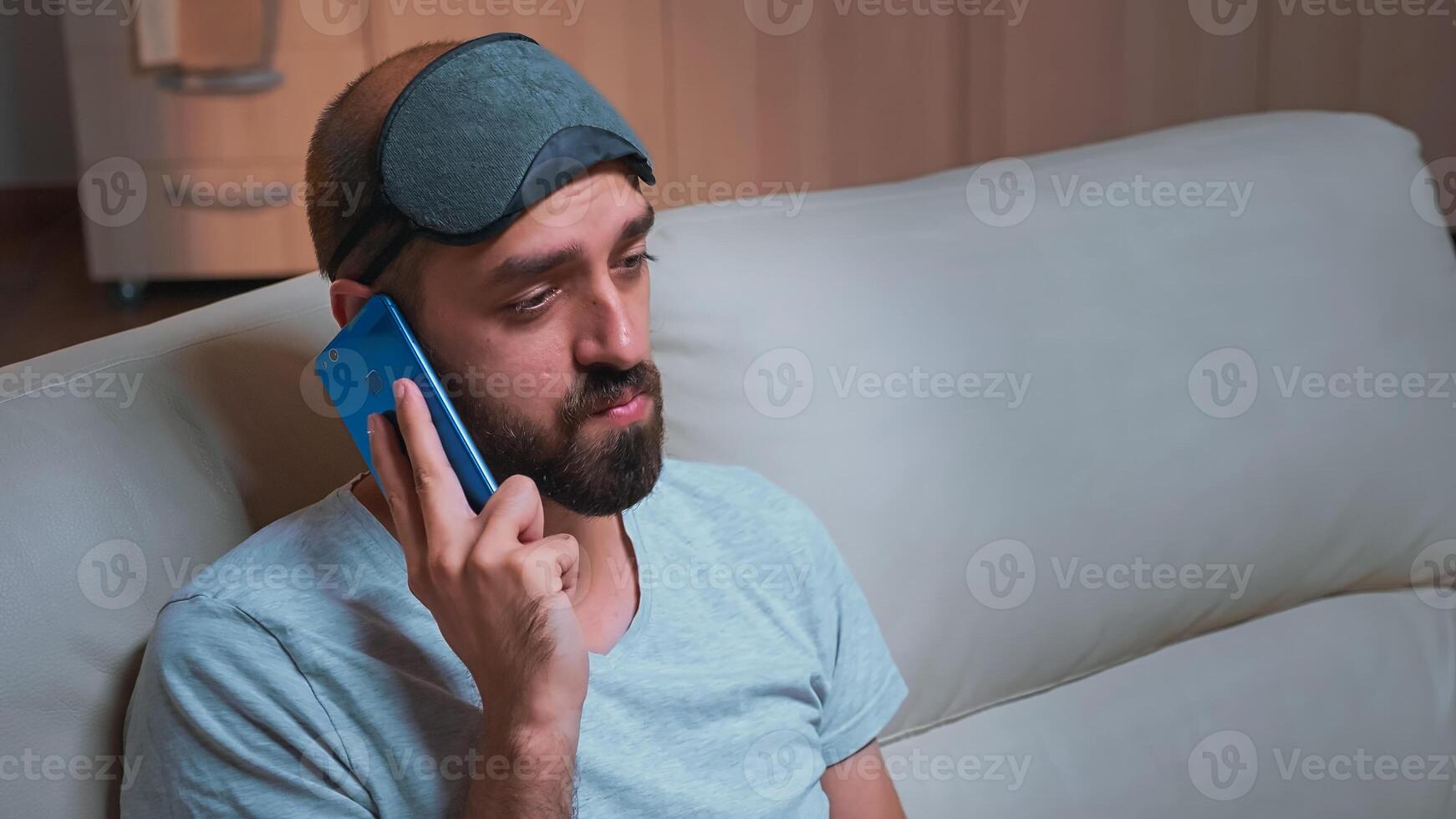 Close up of bored man talking on phone with collegue about social media, holding popcorn bowl in hands. Caucasian male sitting on couch in front of television late at night photo