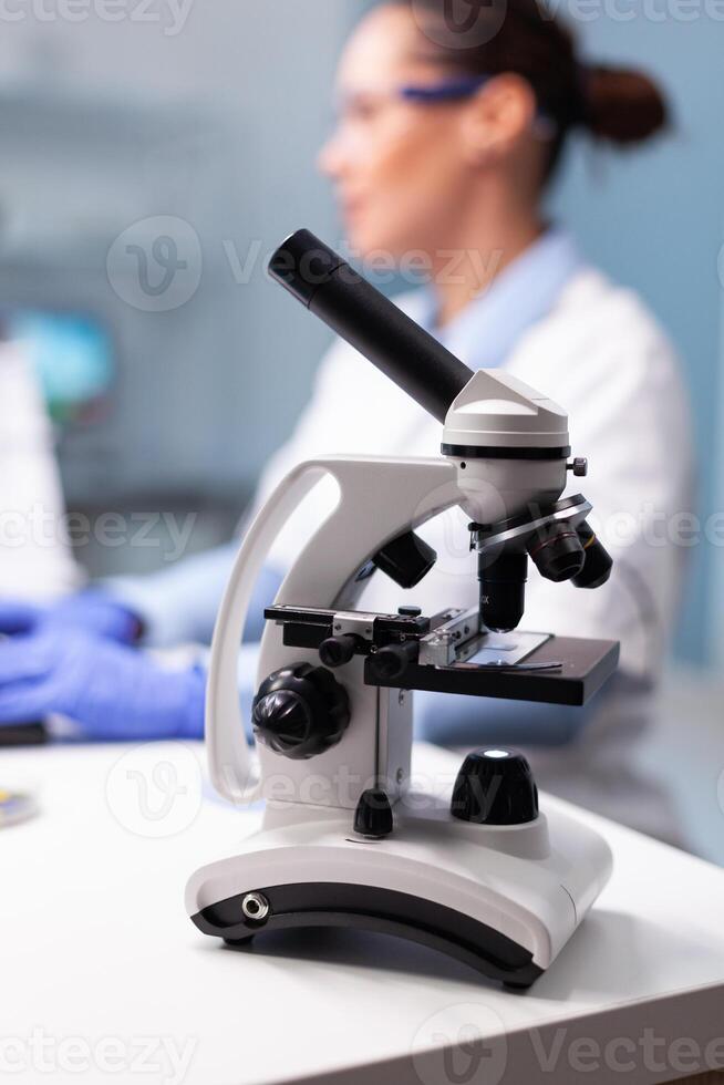 Selectiv focus on medicine microscope standing on table in biochemistry researcher laboratory. Specialist microbiologist woman doctor working at pharmacology experiment typing medical expertise photo