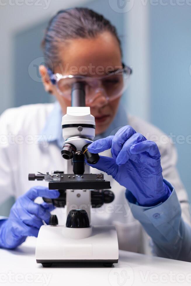 Scientist woman doctor analyzing coronavirus test results using medical microscope discovering pharmaceutical vaccine. Chemist researcher working in biochemistry pharmacology hospital laboratory photo