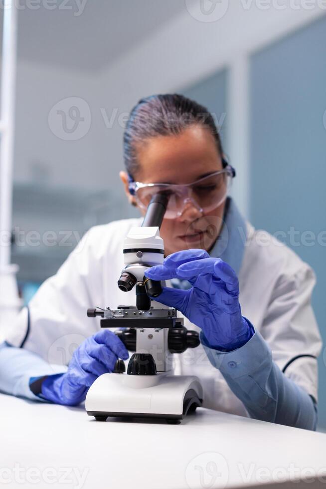 Specialist pharmacist examining bacteriology infection lab test using medical microscope working in pharmacology hospital laboratory. Scientist microbiologist analyzing microbiology expertise photo