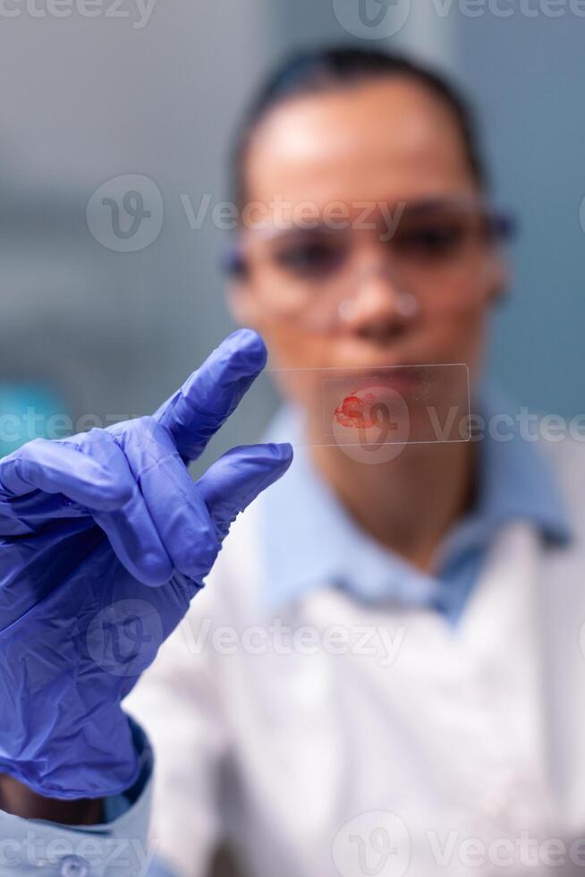 Portrait of specialist doctor analyzing blood sample test working at genetic experiment in biological biochemistry hospital laboratory. Scientist woman researching virus illness environment photo