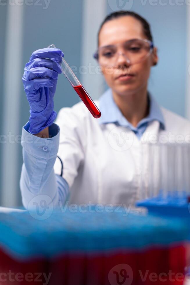 Scientist researcher looking at blood test tube researching scientific biology expertise in discovery laboratory. Specialist chemist working at microbiology experiment discovering disease infection photo