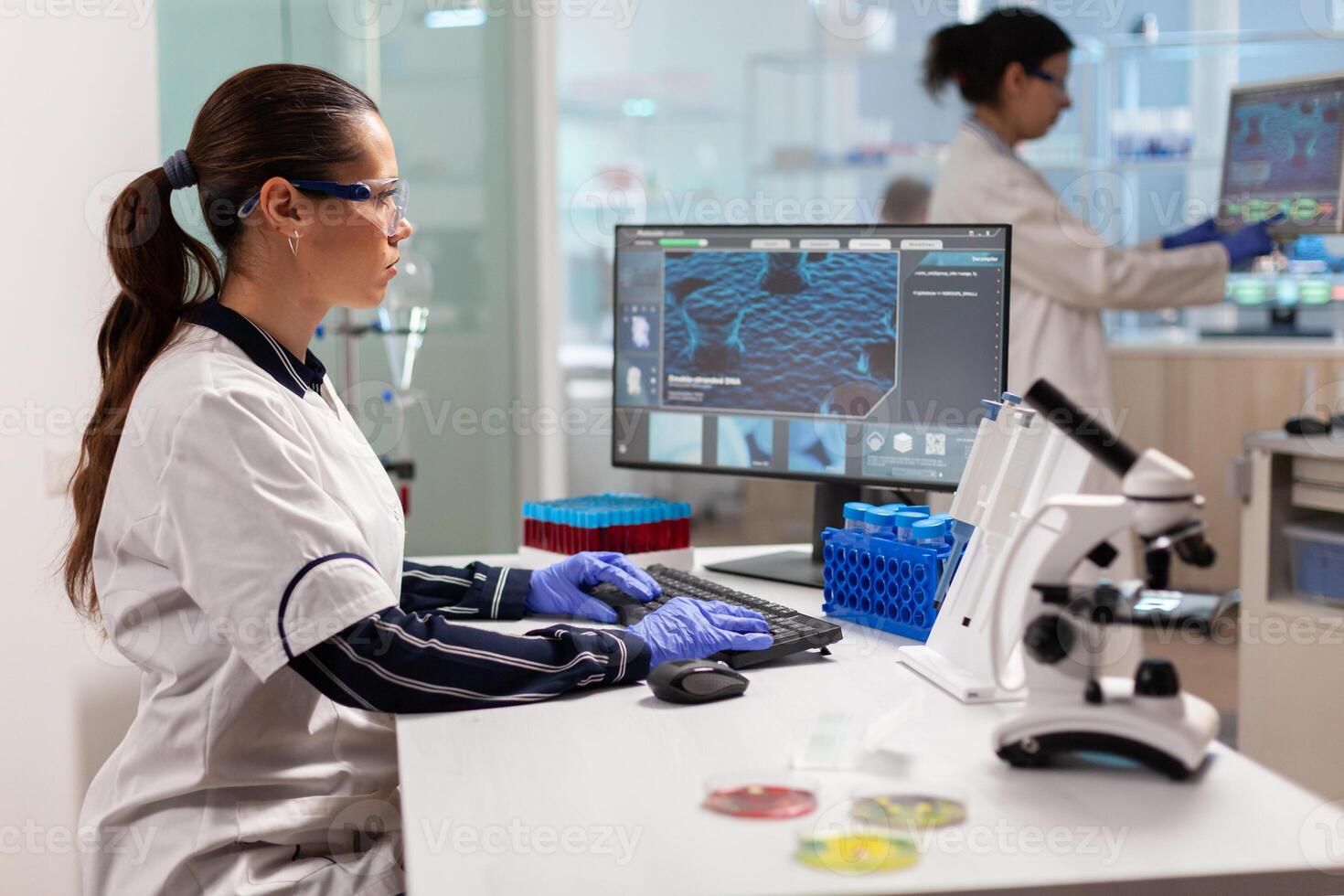 Team working to develop a new vaccine in modern equipped laboratory, typing on computer. Scientists examining vaccine evolution in medical lab using high tech, chemistry tools for scientific research. photo