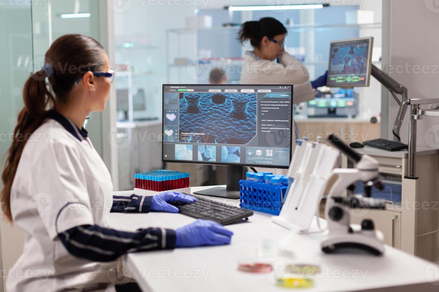 Healthcare researcher working to discover a vaccine working on computer. Scientists examining vaccine evolution in medical lab using high tech, chemistry tools for scientific research. photo