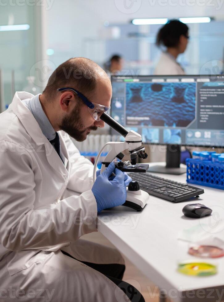 Chemist doctor looking through microscope at virus sample on patient blood to develop vaccine.. Specialists working on medicine, biotechnology research in advanced pharma lab. photo
