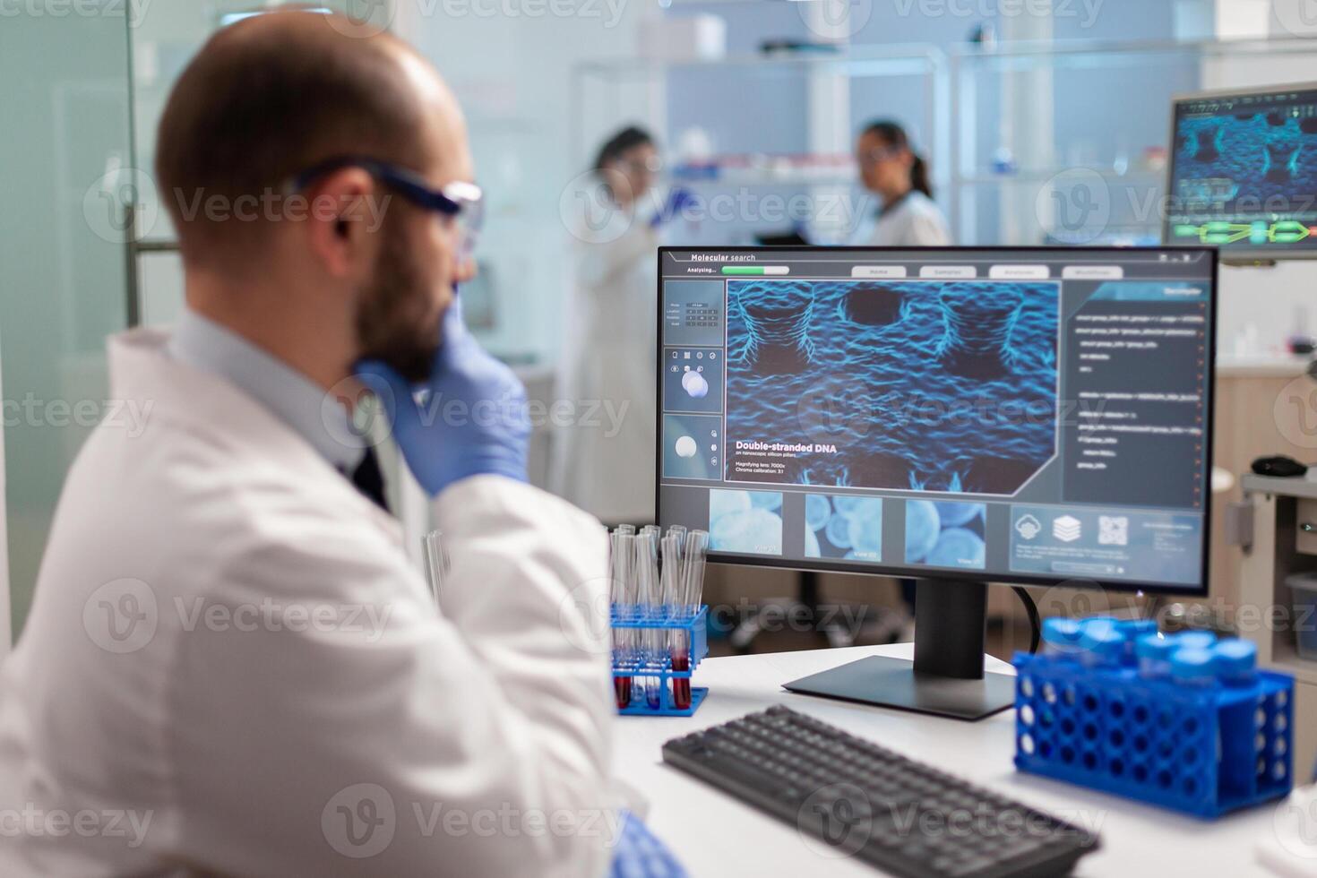 Thoughtfull doctor analyzing virus evolution on computer screen wearing protection glasses. Scientists examining vaccine evolution in medical lab using high tech, chemistry tools for scientific research. photo