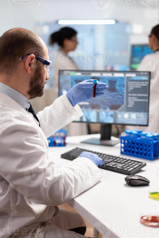 Genetic scientist studying epidemics holding sample of blood in test tube. Viorolog in professional lab analysing vaccine evolution, using modern technology, epidemics, health innovation. photo