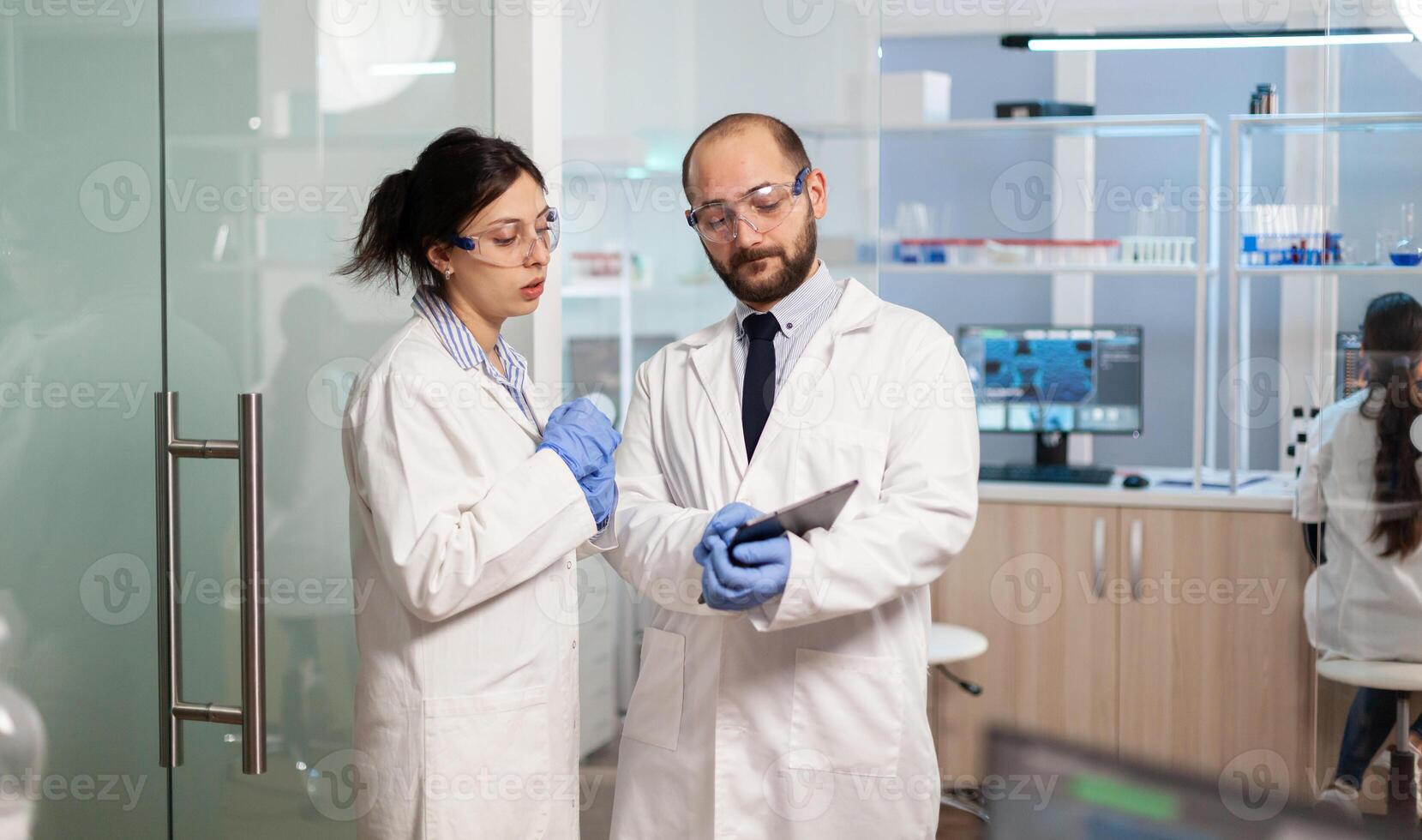 Team of medical scientists conducting vaccine development with help of high tech technology, doctor holding tablet analysing new informations. Examining virus evolution using devices researching diagnosis. photo