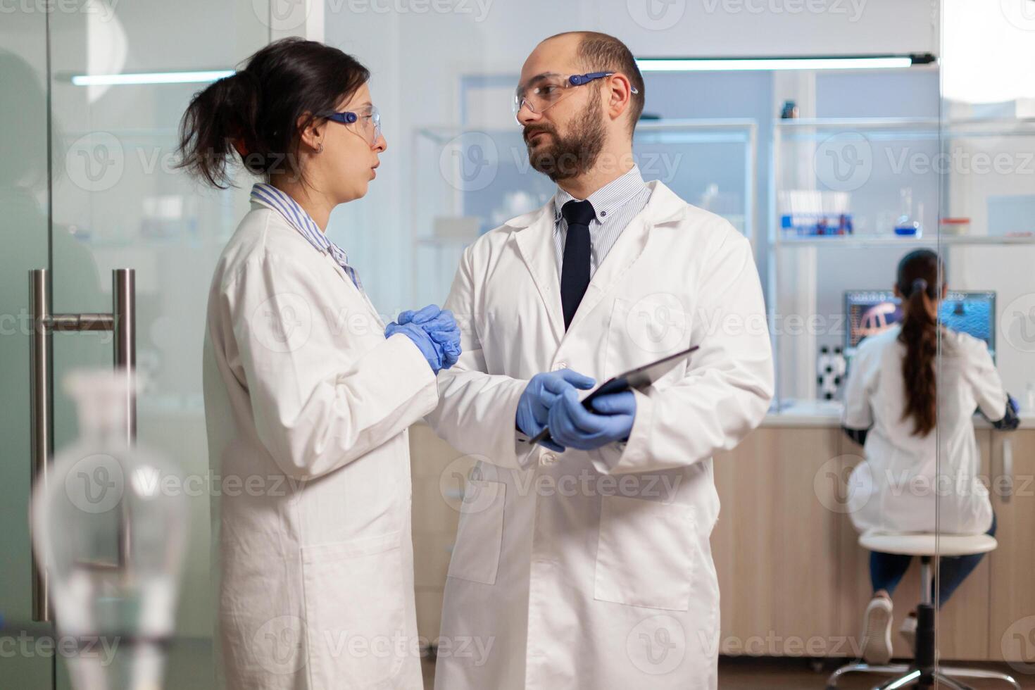 Scientists coworkers using digital tablet working in medical research laboratory, analysing biochemicals samples, talking. Scientific lab for medicine, microbiology development with advanced equipment. photo