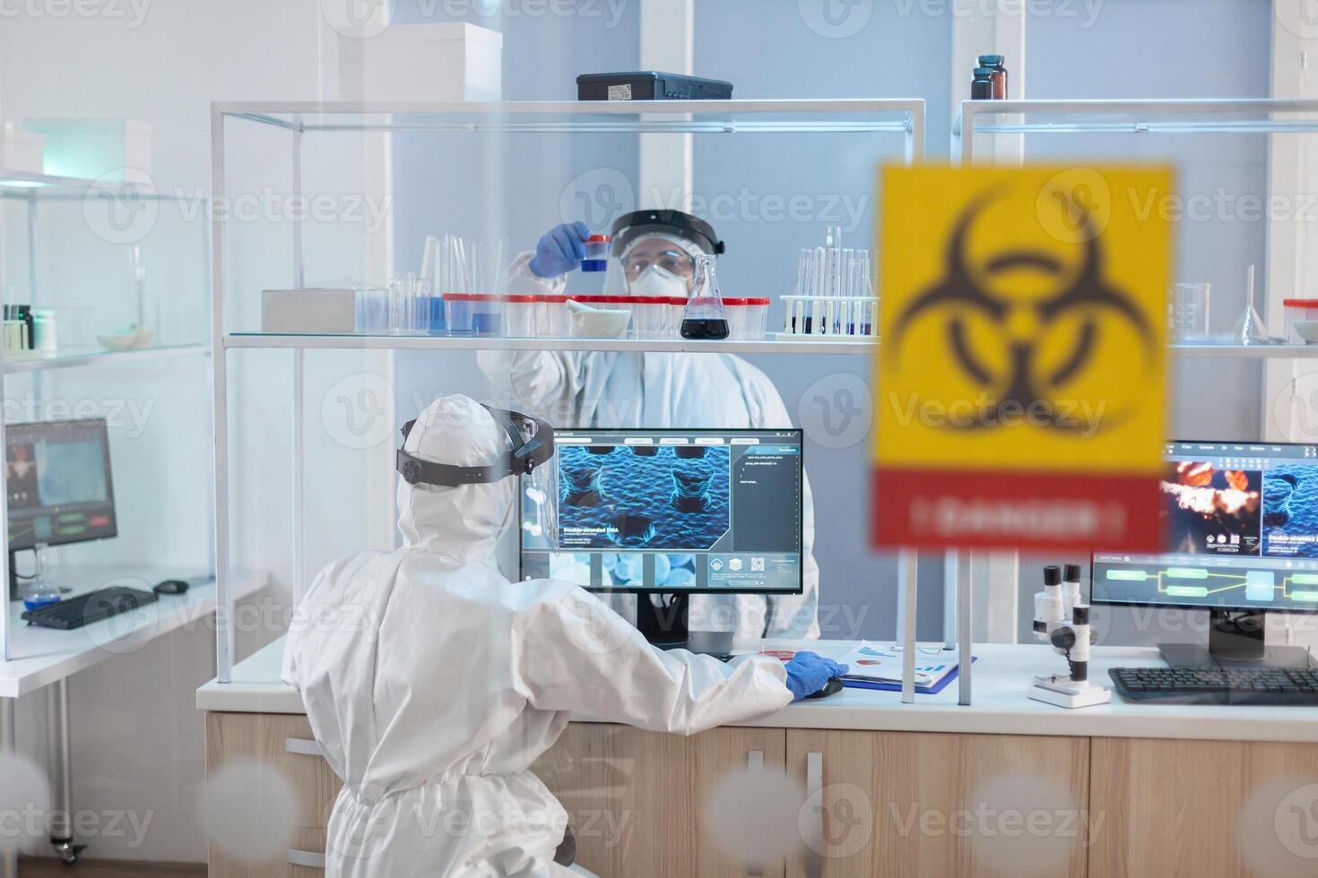 Medical staff wearing ppe suit in laboratory danger zone during pandemic. Group of doctors examining vaccine evolution using high tech for diagnosis against covid19. photo