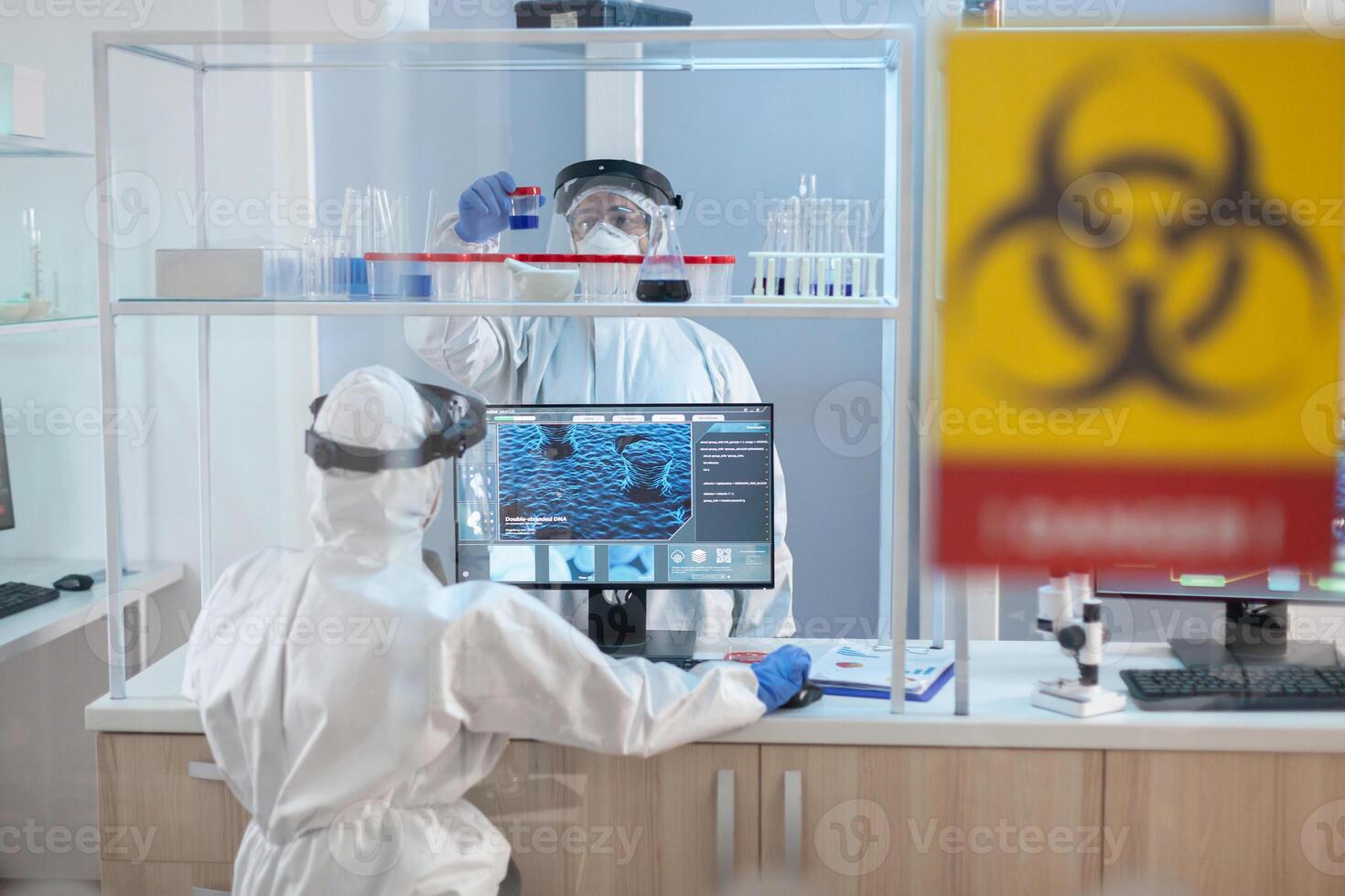 Team of scientist working to develope treatment for virus in lab dresed in ppe suit. Group of doctors examining vaccine evolution using high tech for diagnosis against covid19. photo