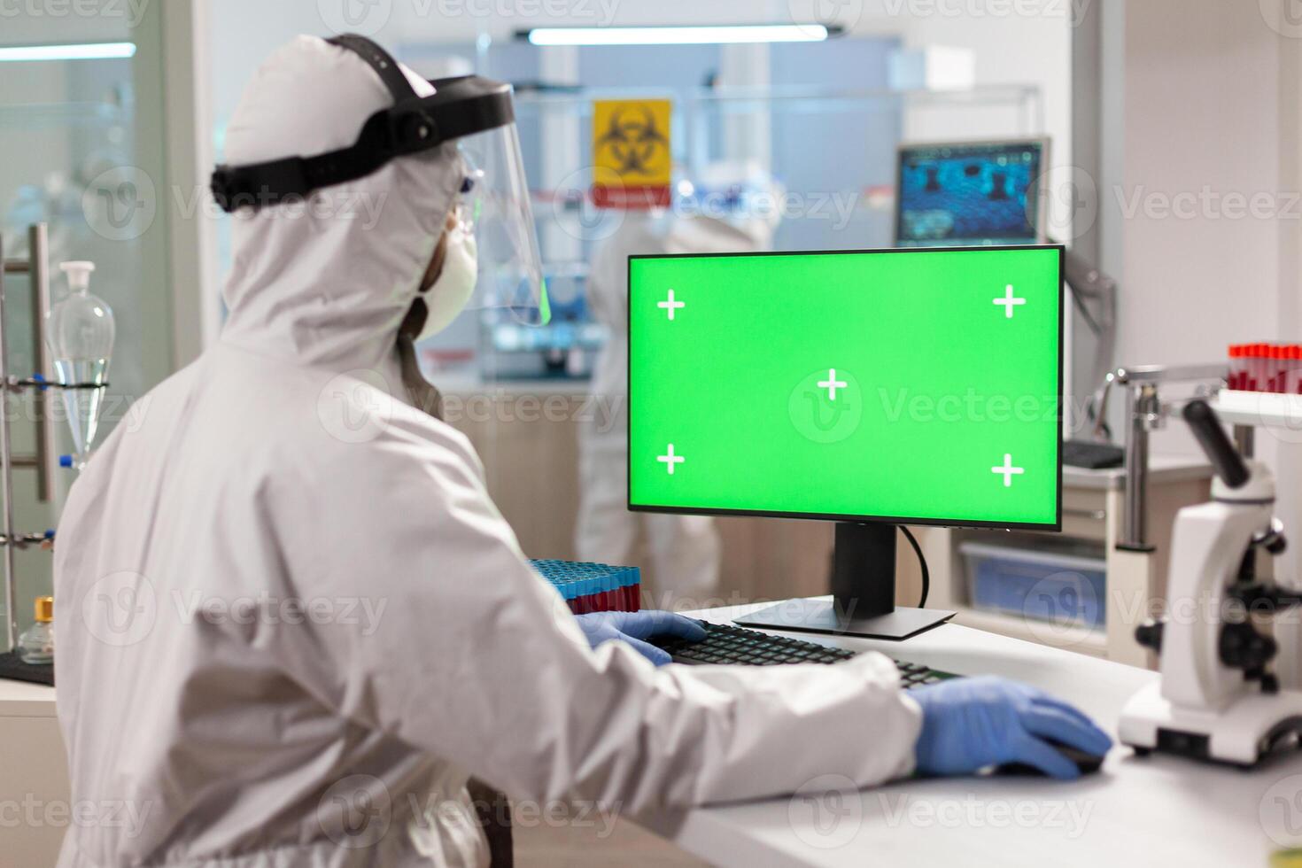 Man researcher in coverall looking at chroma key computer in modern equipped lab. Team of microbiologists doing vaccine research writing on device with chroma key, isolated display. photo