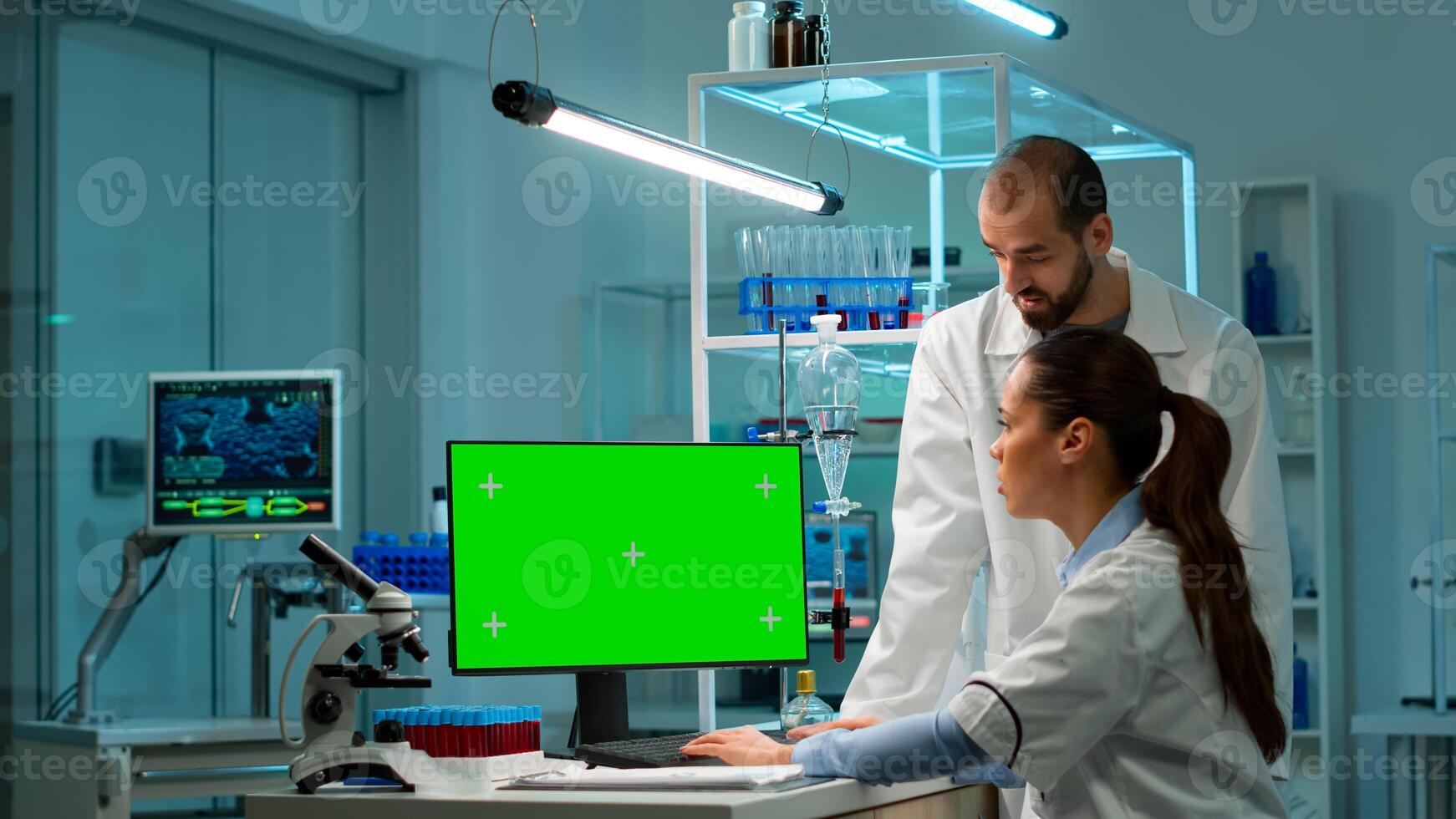 Professional chemists working on computer with green screen mock up and testing virus evolution, developing vaccine, drugs and antibiotics. Standing in high tech laboratory with chroma key display photo